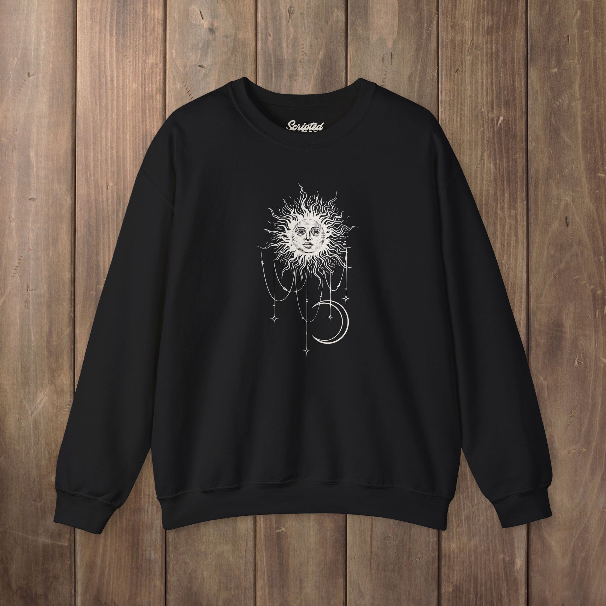Black crewneck sweatshirt with boho celestial sun face, stars, and crescent moon design worn by Patricia in Widow's Bay