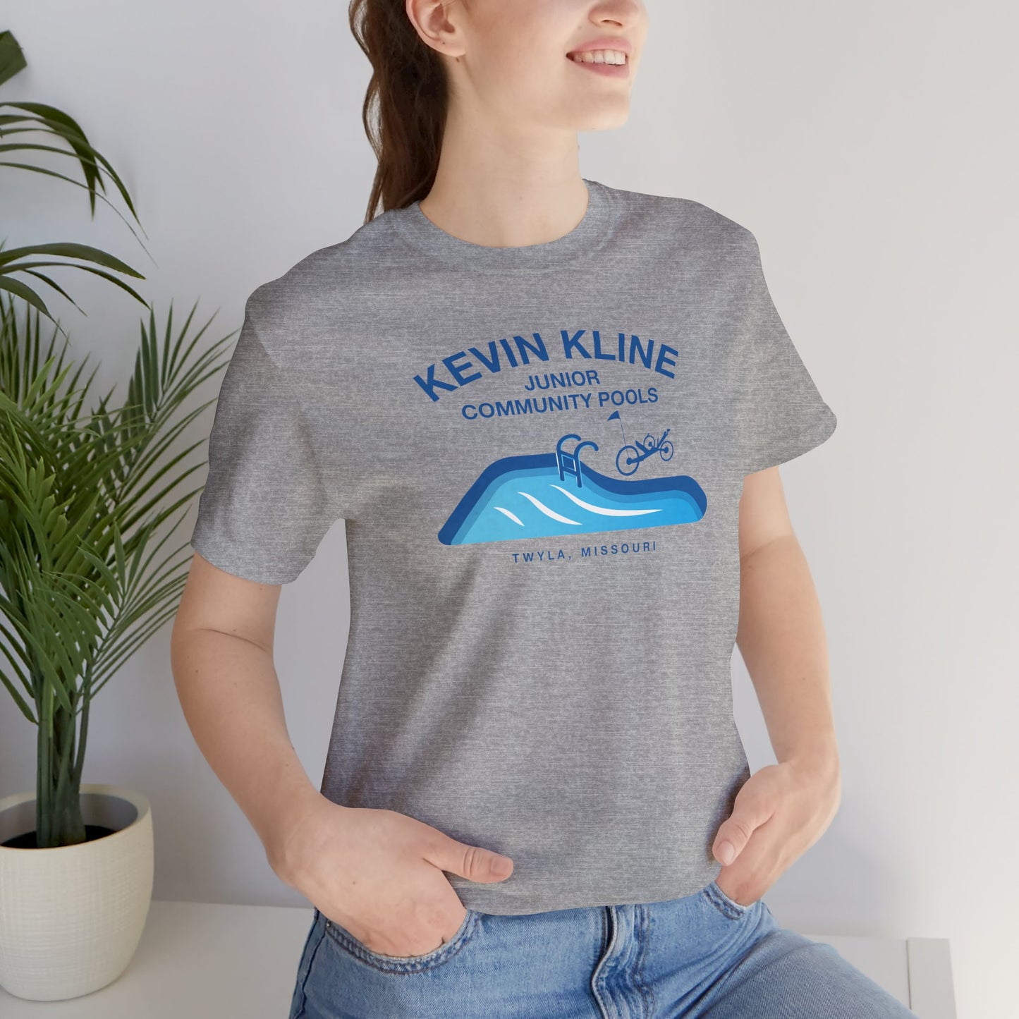 Woman wearing heather gray DTF St. Louis Kevin Kline Junior Community Pools graphic tee with pool and recumbent trike.