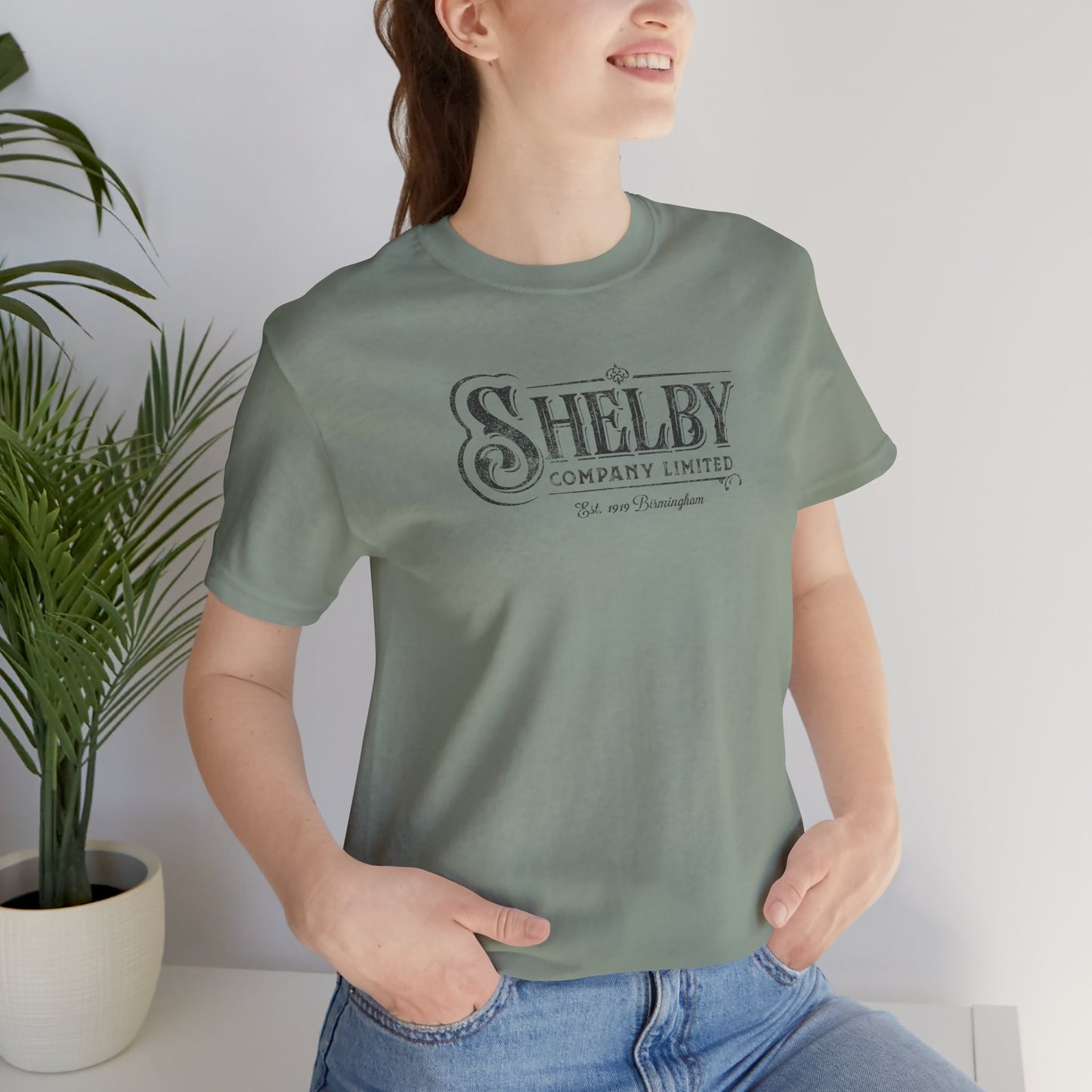 Woman wearing sage green Bella+Canvas 3001 t-shirt featuring a vintage Shelby Company Limited logo from Peaky Blinders.