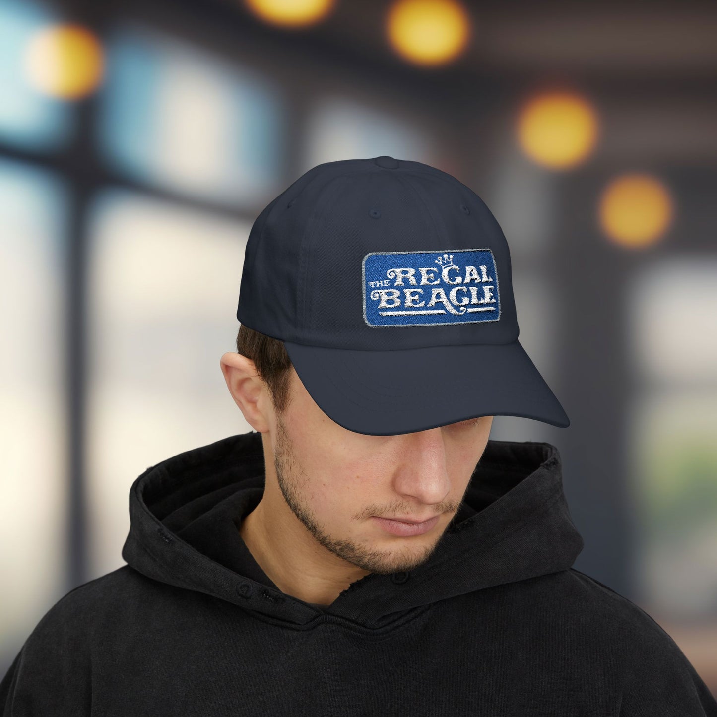 Person wearing navy blue dad cap with embroidered Regal Beagle patch logo, Three's Company inspired fictional bar merch
