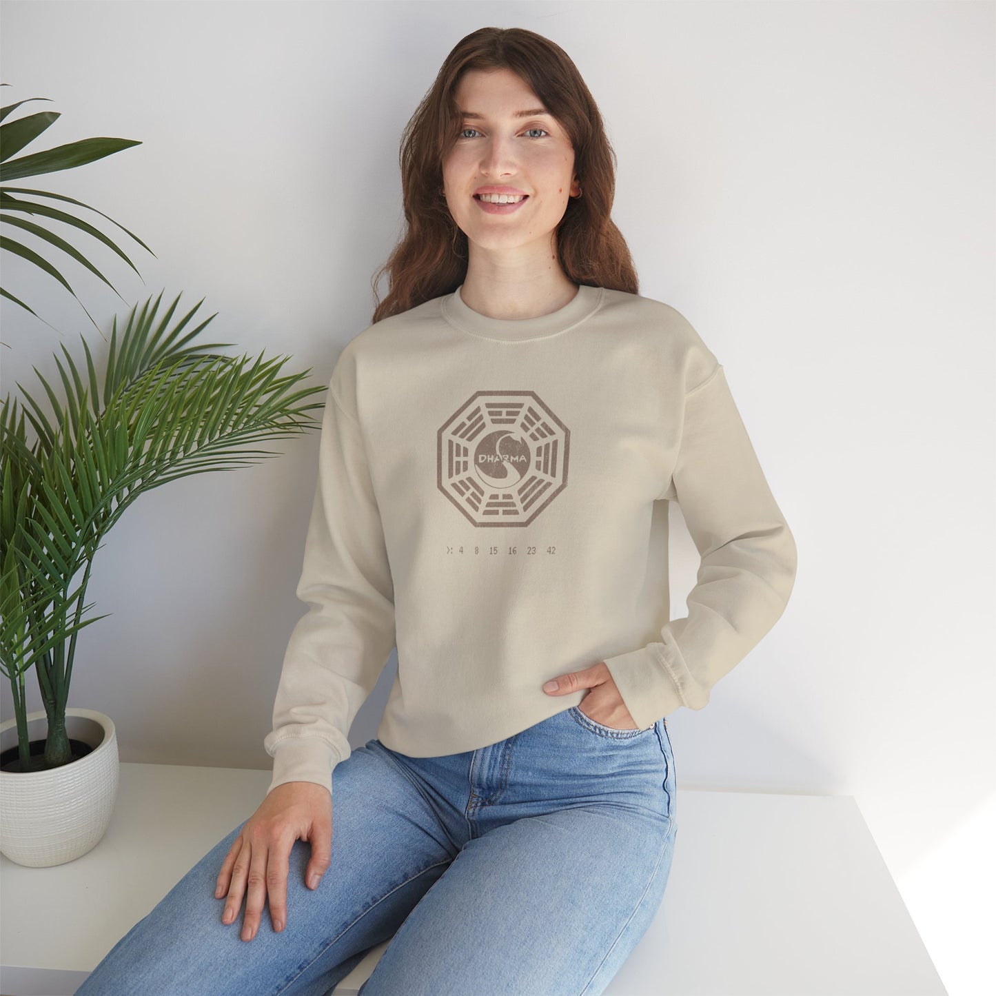 Model wearing a sand Soft Gildan 18000 crew neck sweatshirt featuring the Dharma Initiative swan logo graphic from the TV show LOST in a vintage distressed ink-stamped worn-in style.