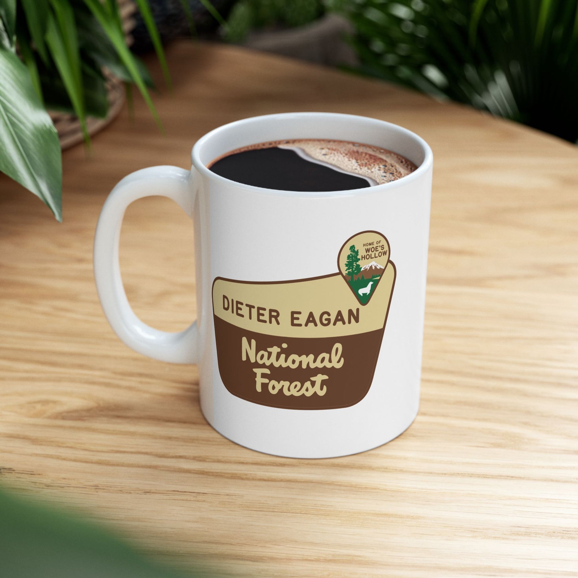 11 oz White ceramic mug with Dieter Eagan National Forest logo, inspired by Woe’s Hollow episode in Severance, shown on a table.