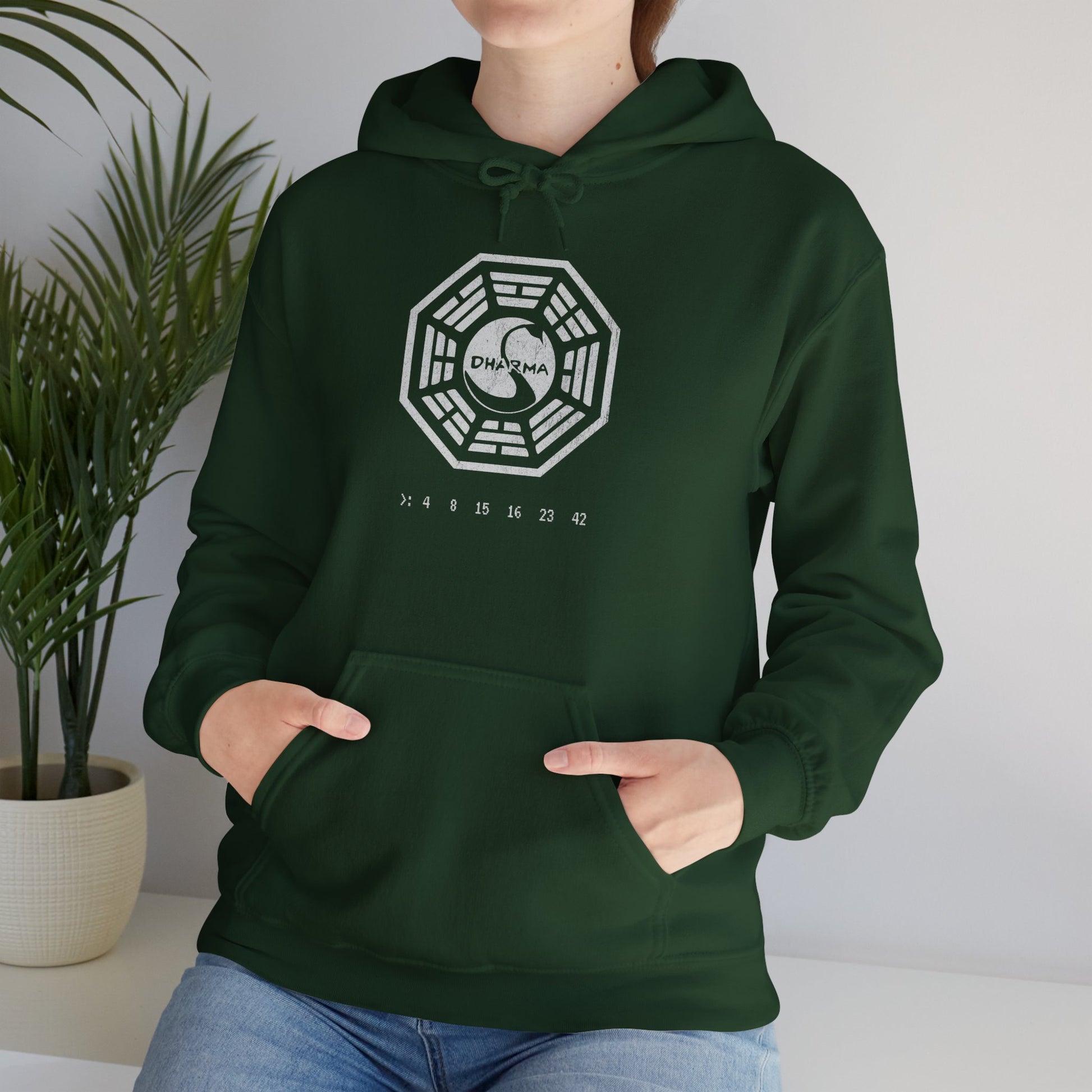 Female model wearing a forest green Unisex Hoodie Heavy Blend Hooded Sweatshirt featuring the Dharma Initiative swan logo graphic from the TV show LOST in a vintage distressed ink-stamped worn-in style.