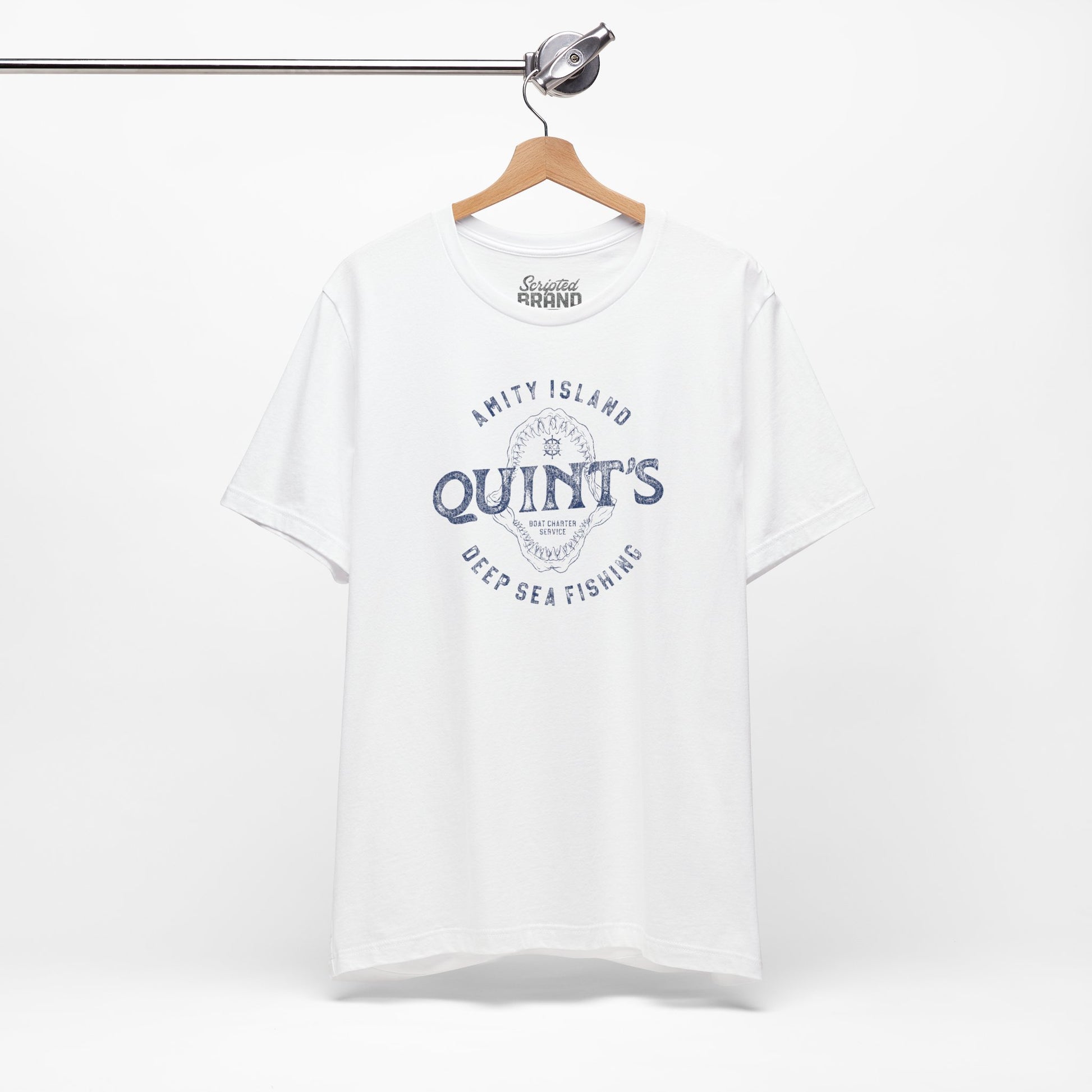 White colored Soft short-sleeve t-shirt on a hanger featuring the Quint's Deep Sea Fishing Boat Charters logo graphic inspired by the movie Jaws in a vintage distressed ink-stamped worn-in style.