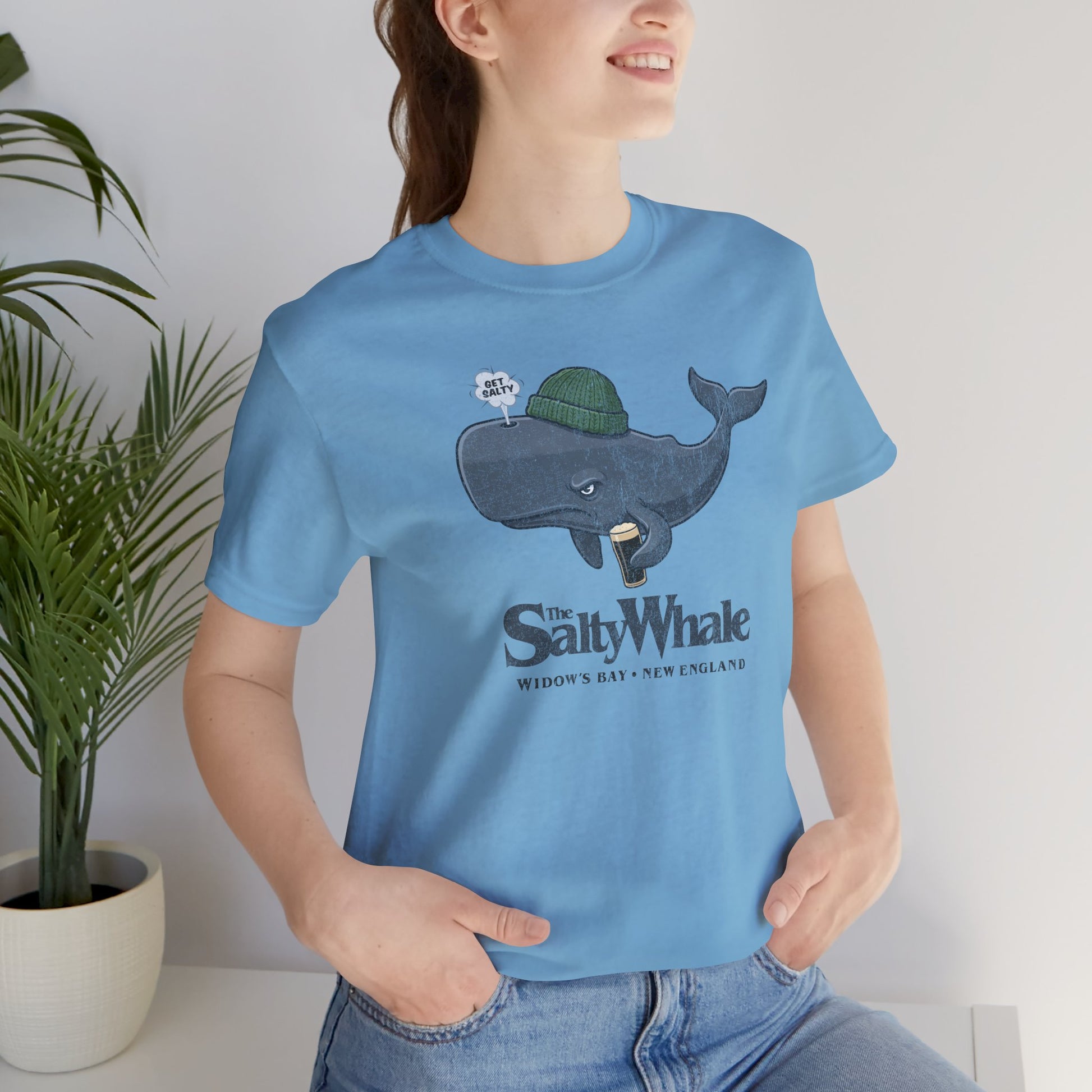 Woman wearing Ocean blue 'The Salty Whale' cartoon mascot t-shirt inspired by Widow's Bay Apple TV series, soft Bella+Canvas cotton pub fan tee