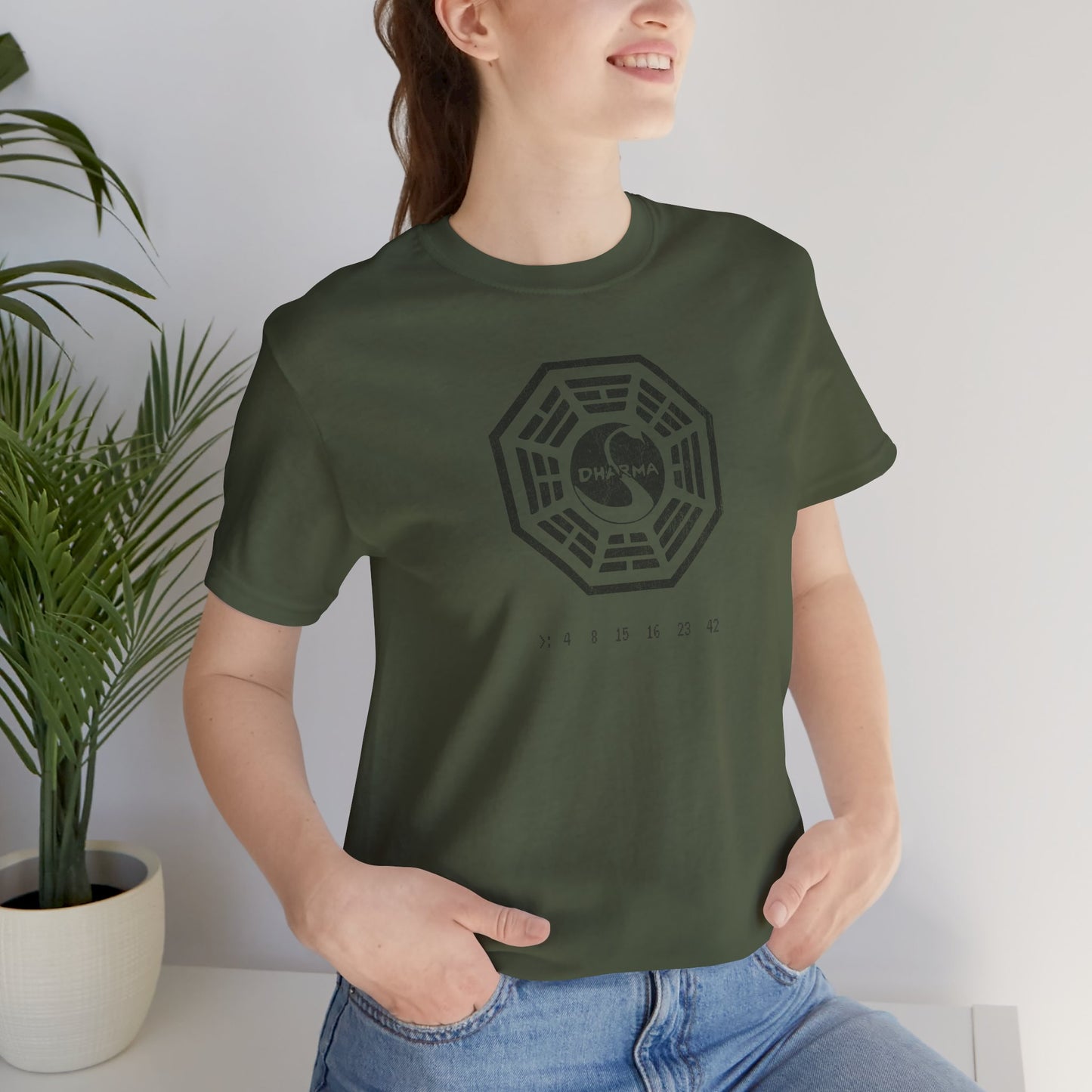 Female model wearing a military green short-sleeve t-shirt featuring the Dharma Initiative swan station logo graphic from the TV show LOST in a vintage distressed  style.