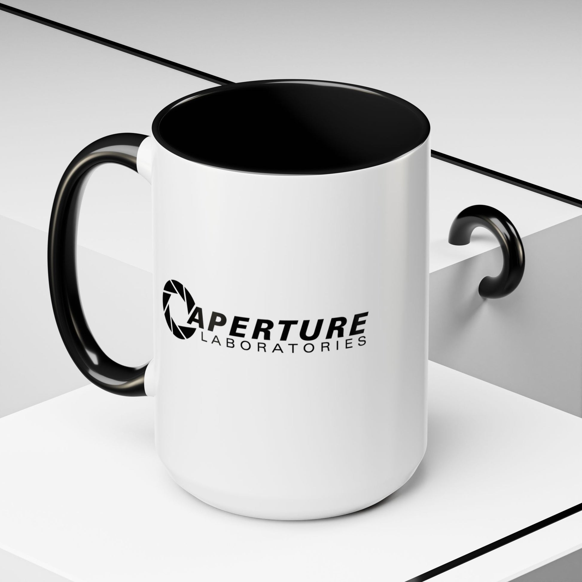 Front angled view of a 15 oz white Ceramic Accent Mug with the black Aperture Laboratories logo from the video game Portal on both sides. Handle and interior are colored black.