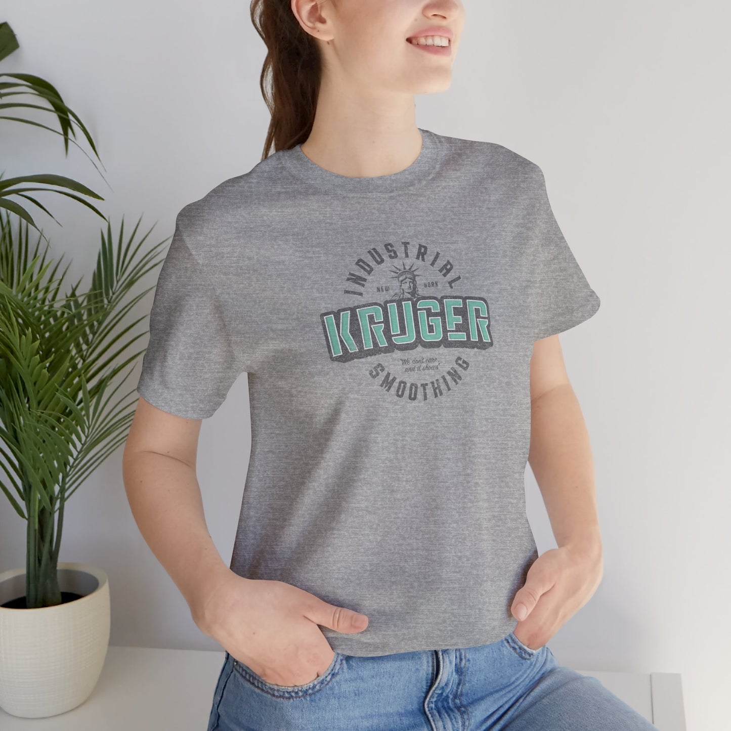 Female model wearing an athletic heather grey colored Soft unisex Bella+Canvas 3001 short-sleeve t-shirt featuring a Kruger Industrial Smoothing logo graphic in a vintage distressed style, designed by ScriptedBrand, and  inspired by the TV show Seinfeld.