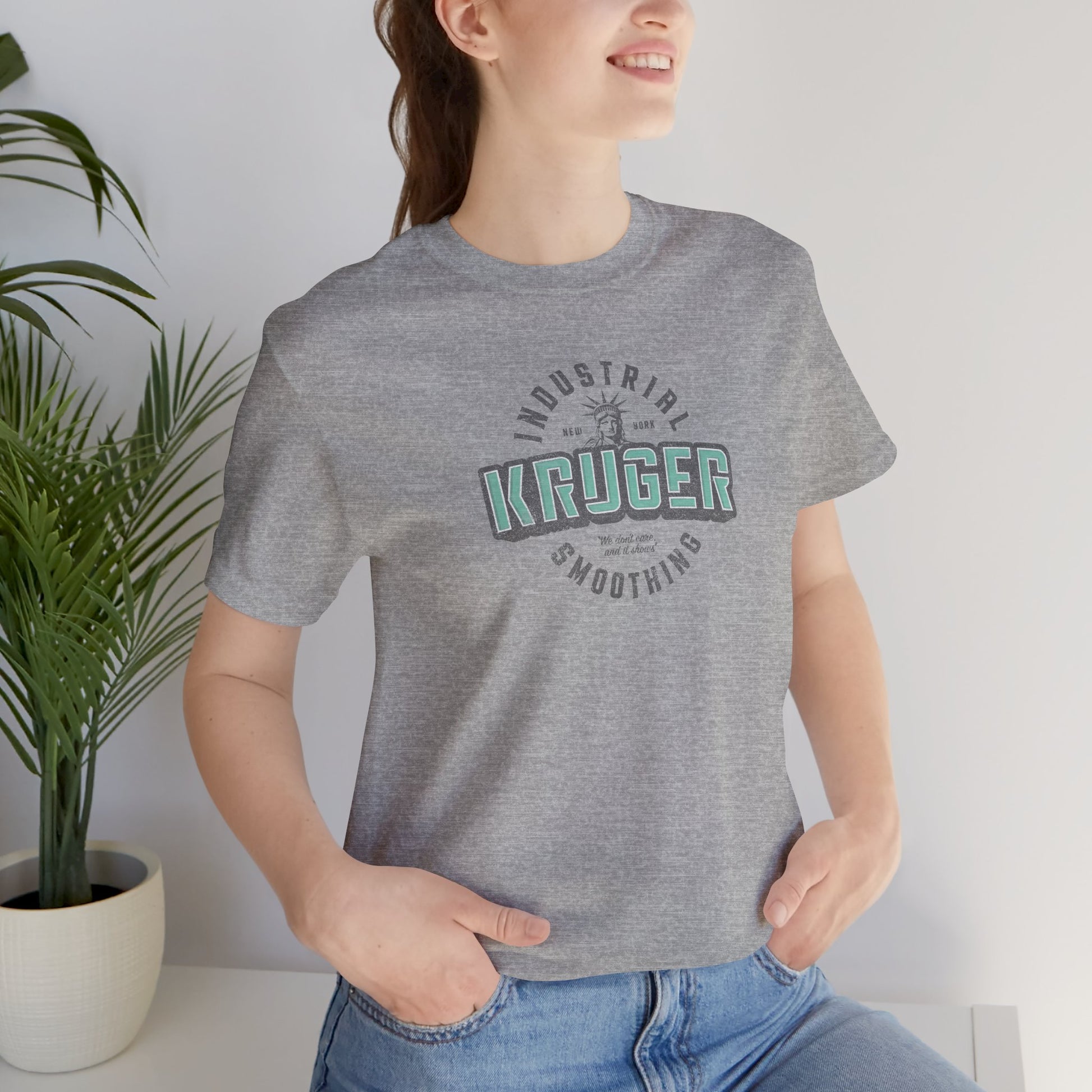 Female model wearing an athletic heather grey colored Soft unisex Bella+Canvas 3001 short-sleeve t-shirt featuring a Kruger Industrial Smoothing logo graphic in a vintage distressed style, designed by ScriptedBrand, and  inspired by the TV show Seinfeld.