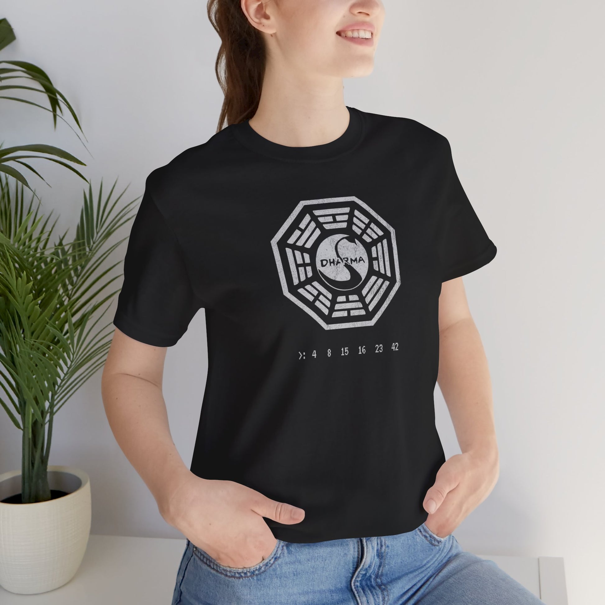 Female model wearing a Black short-sleeve t-shirt featuring the Dharma Initiative swan station logo graphic from the TV show LOST in a vintage distressed  style.
