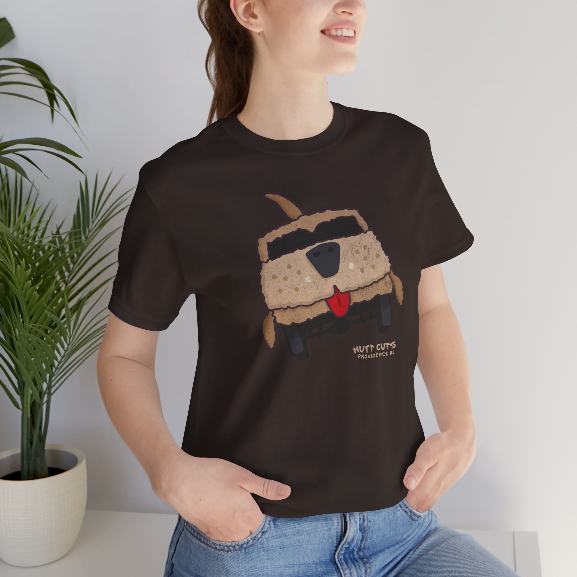 Woman wearing brown Bella+Canvas tee with vintage Mutt Cutts dog van graphic inspired by Dumb and Dumber movie.