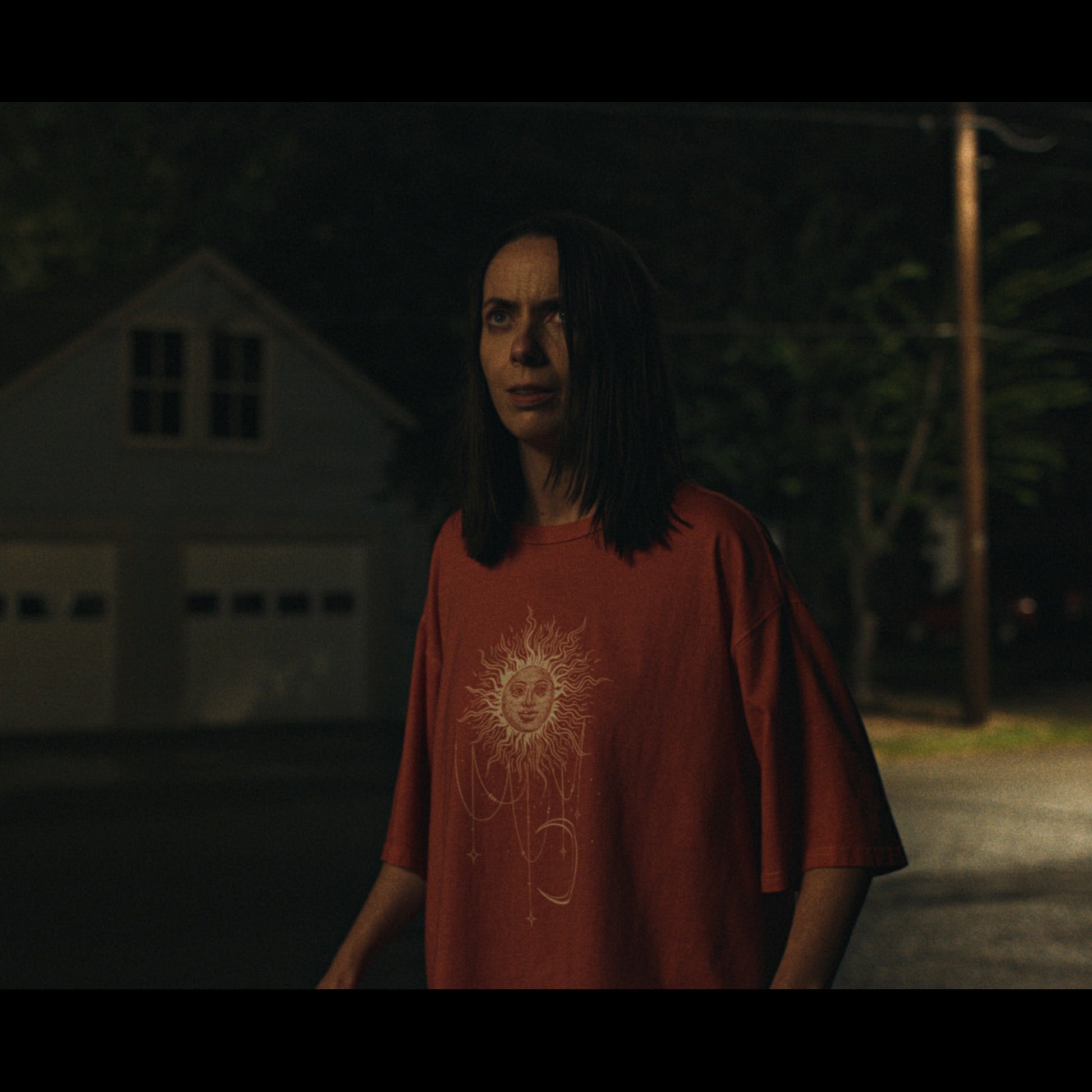 Person wearing a red t-shirt with a sun design in a dark setting