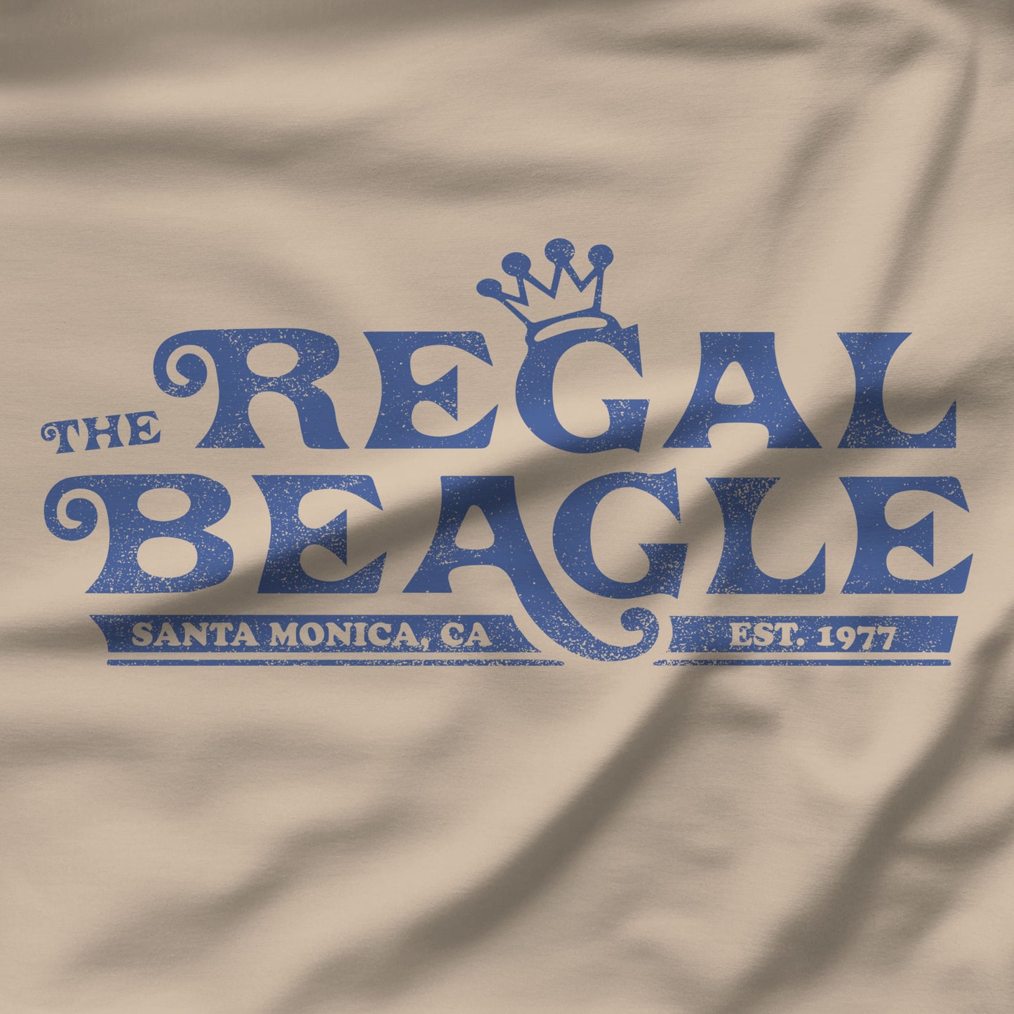 Closeup of Sand beige crewneck sweatshirt with vintage distressed blue Regal Beagle Three's Company logo