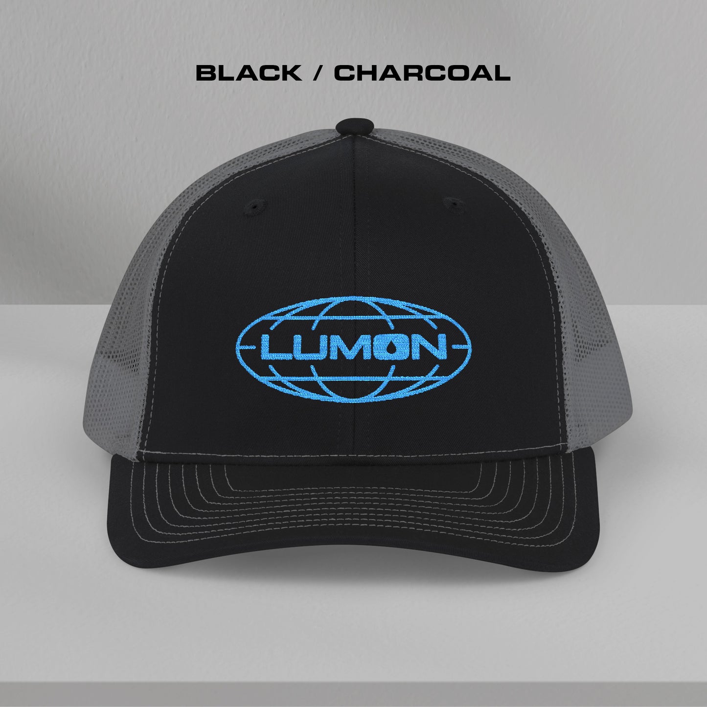 Front view of a black and charcoal Richardson 112 trucker cap with embroidered blue Lumon Industries logo inspired by Severance.