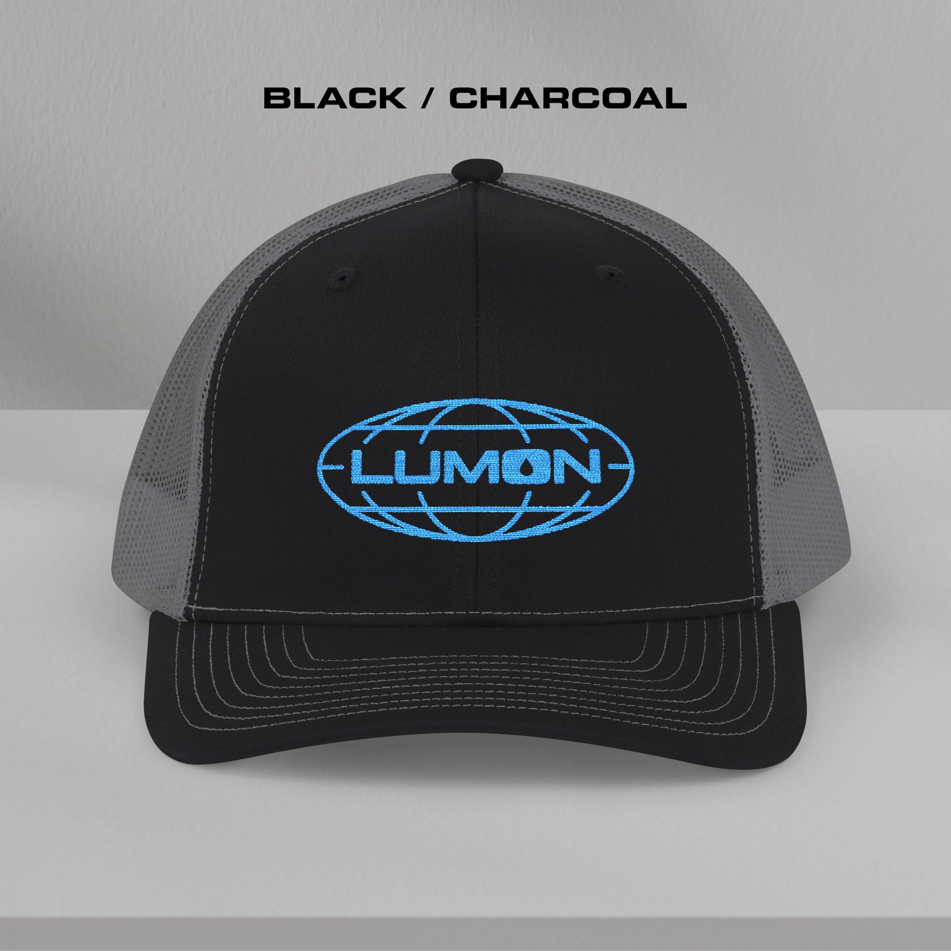 Front view of a black and charcoal Richardson 112 trucker cap with embroidered blue Lumon Industries logo inspired by Severance.