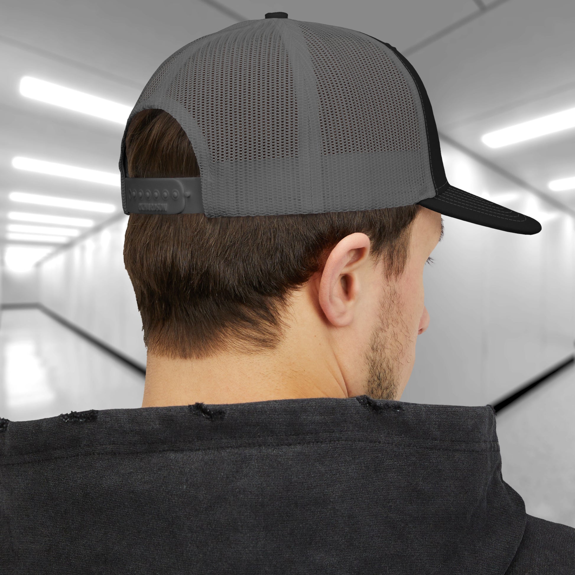 Back view of man wearing black and charcoal Richardson 112 trucker cap with embroidered blue Lumon Industries logo inspired by Severance.