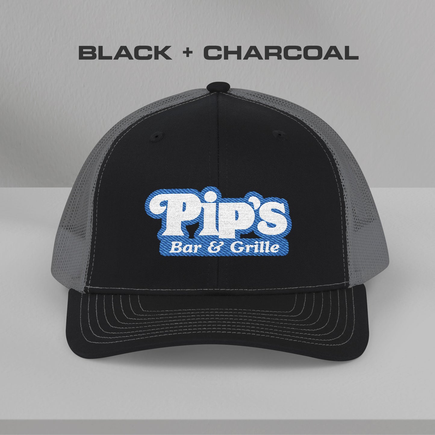 Front view of black and charcoal Richardson 112 trucker hat with embroidered Pip’s Bar & Grille logo inspired by Severance.
