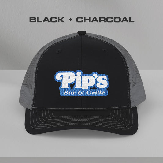 Front view of black and charcoal Richardson 112 trucker hat with embroidered Pip’s Bar & Grille logo inspired by Severance.