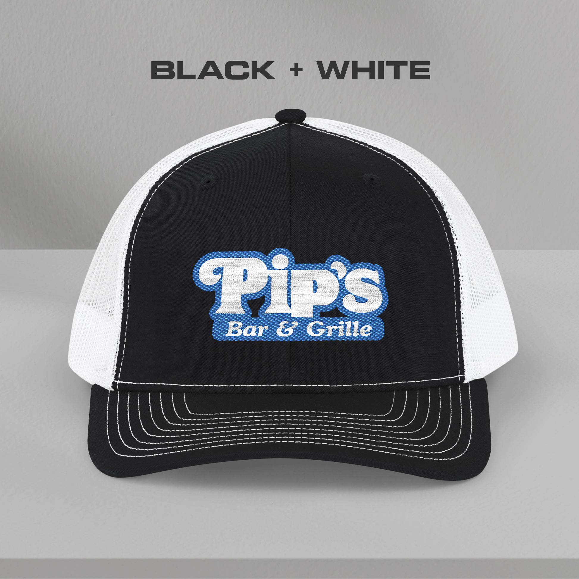 Front view of black and white Richardson 112 trucker hat with embroidered Pip’s Bar & Grille logo inspired by Severance.