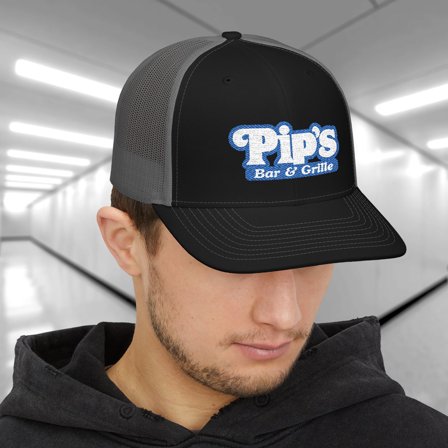 Man wearing black and charcoal Richardson 112 trucker hat with embroidered Pip’s Bar & Grille logo inspired by Severance.