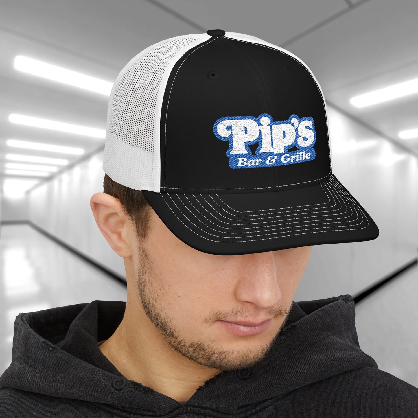 Man wearing black and white Richardson 112 trucker hat with embroidered Pip’s Bar & Grille logo inspired by Severance.