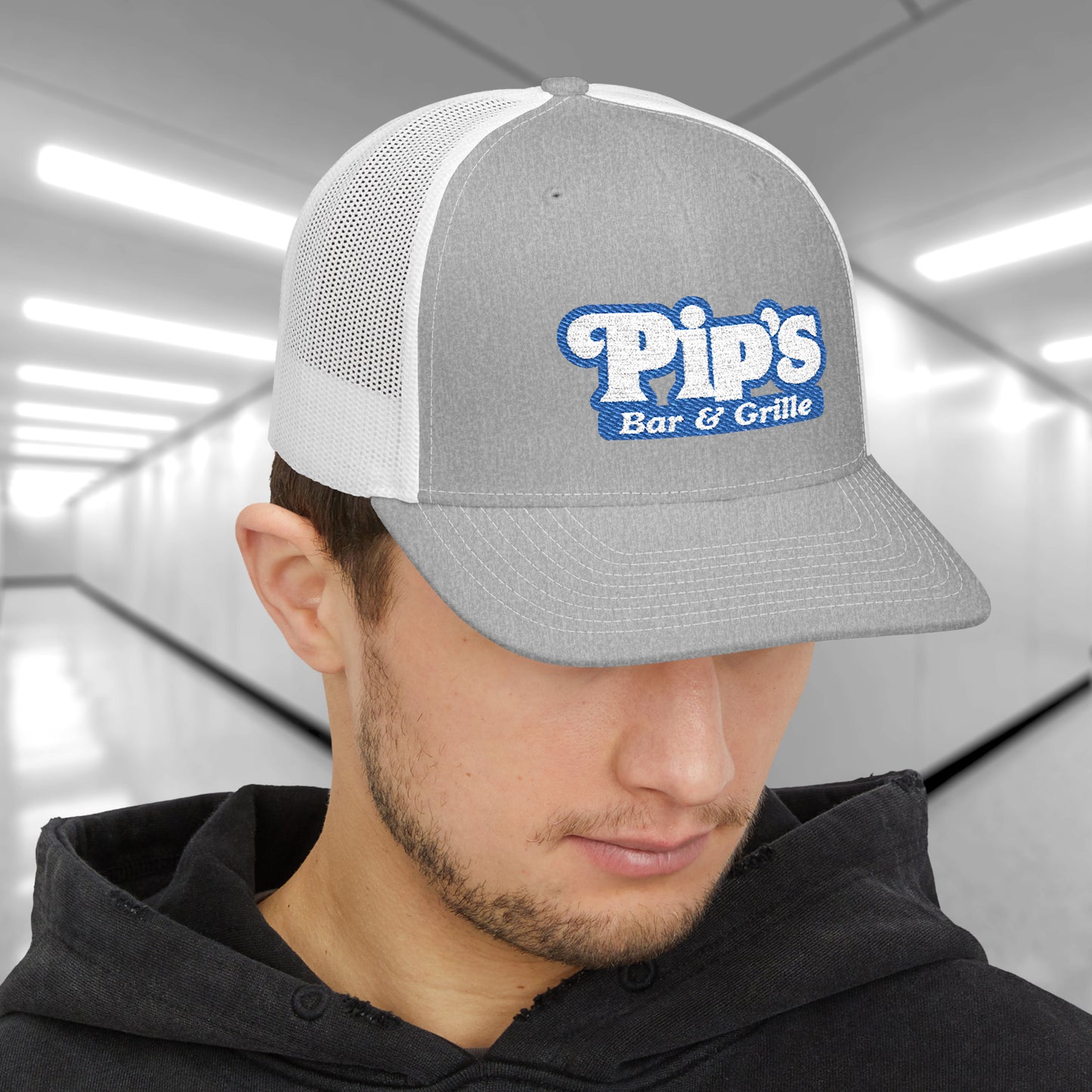 Man wearing gray and white Richardson 112 trucker hat with embroidered Pip’s Bar & Grille logo inspired by Severance.