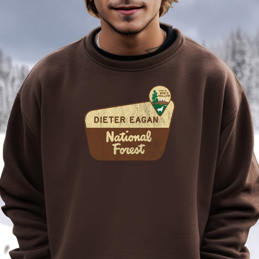 Male Model wearing a dark chocolate brown Soft Unisex Gildan 18000 sweatshirt featuring a logo graphic of the Dieter Eagan National Forest sign designed by ScriptedBrand, inspired by the TV show Severance in a vintage distressed style.