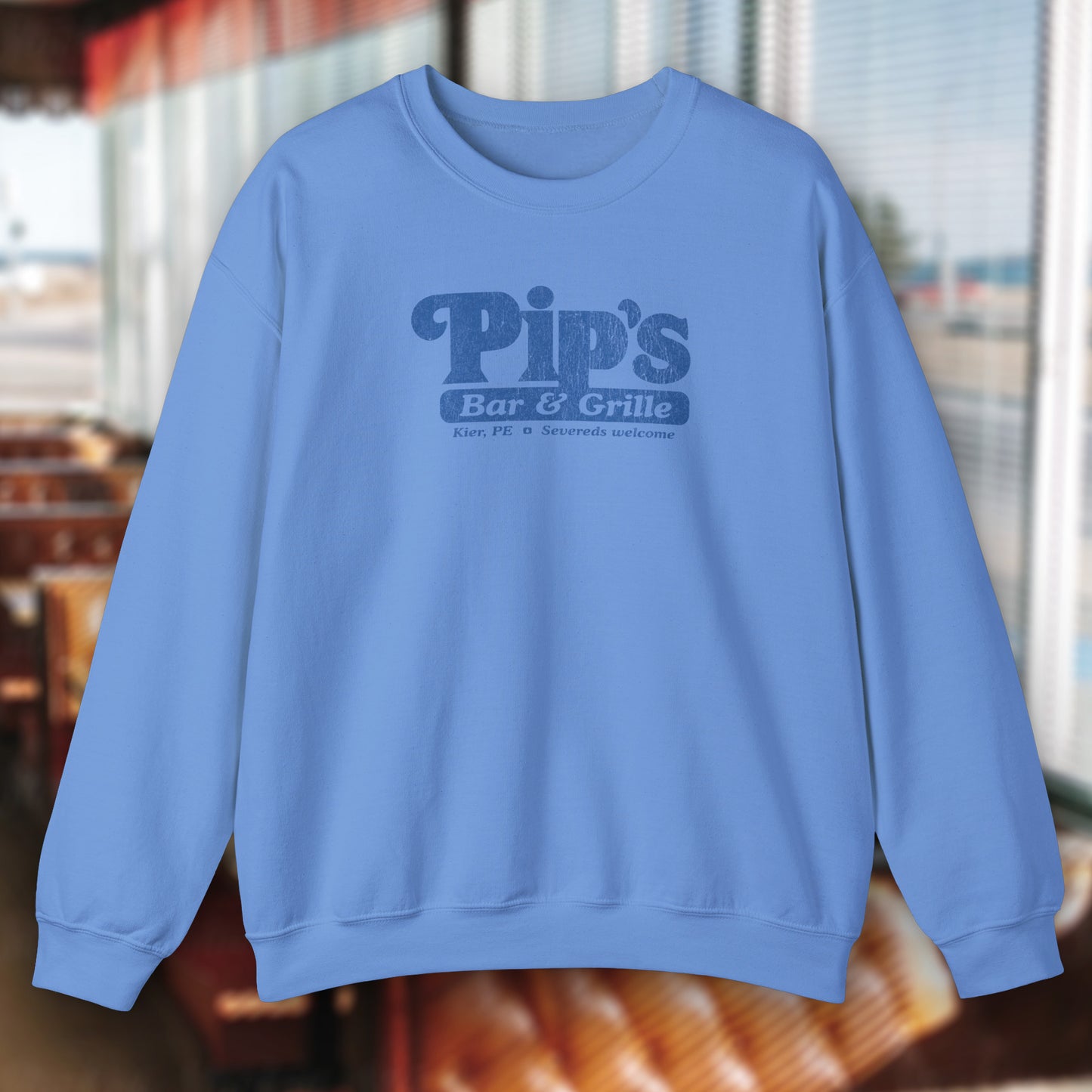 Carolina blue Soft Gildan 18000 sweatshirt featuring the Pips Bar and Grill logo Severeds Welcome from the TV show Severance in a vintage distressed ink-stamped worn-in style.