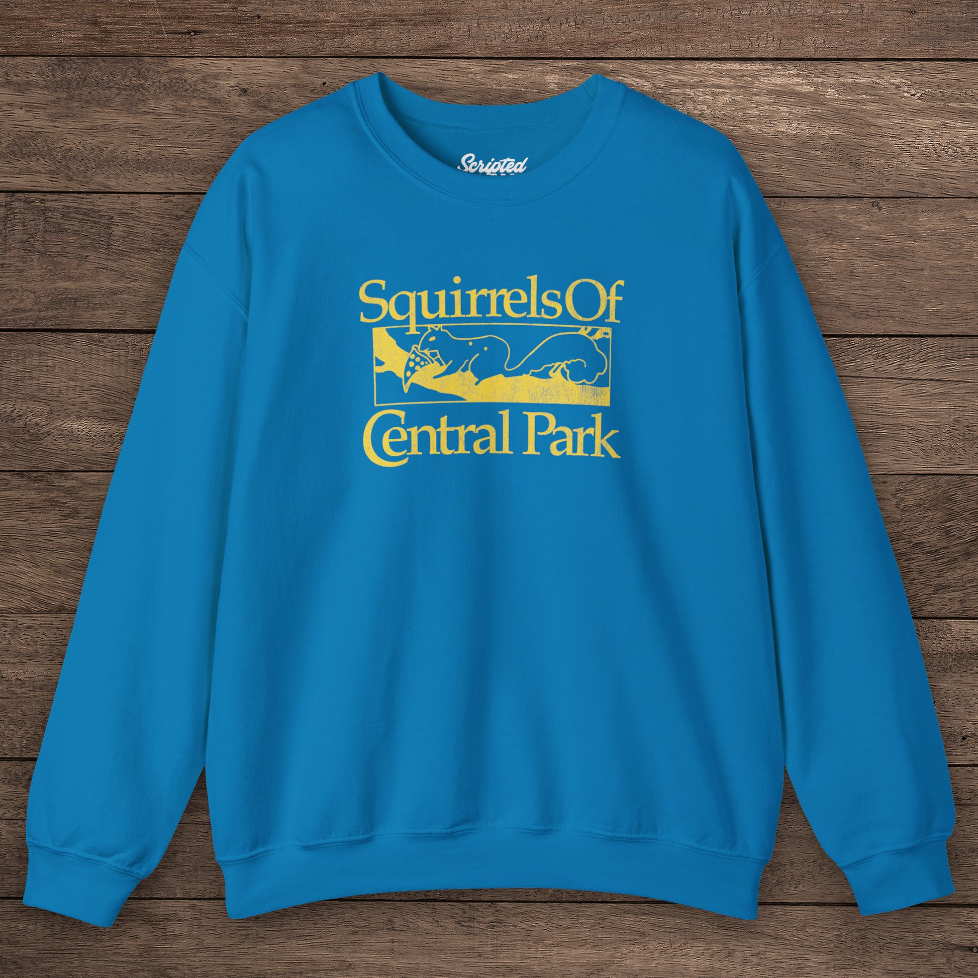 Sapphire blue Squirrels Of Central Park vintage distressed crewneck sweatshirt inspired by Bad Sisters, shown on wooden background.