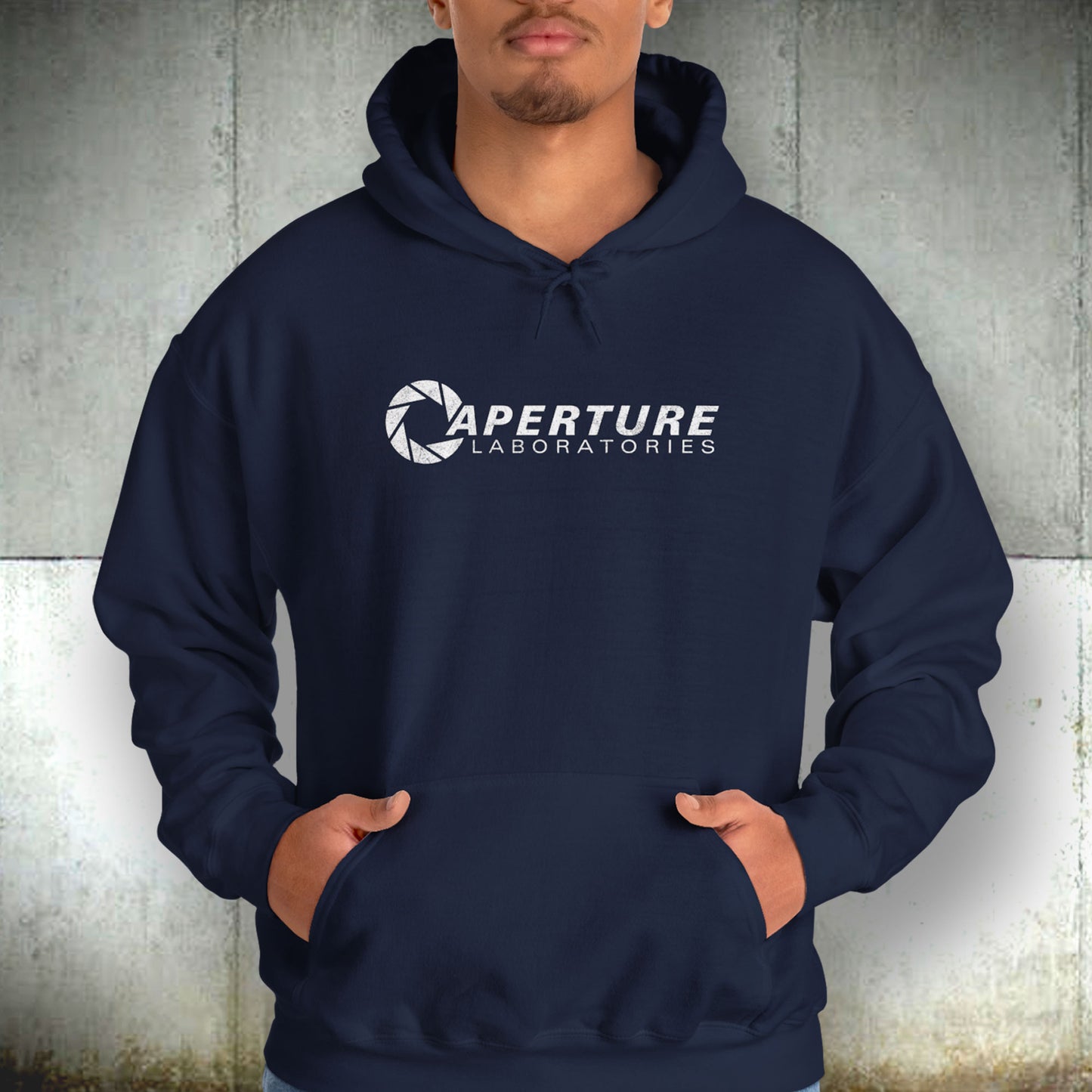 Male model wearing a navy blue colored Unisex Hoodie Heavy Blend Hooded Sweatshirt featuring the Aperture Laboratories logo from the video game Portal and Portal 2 in a vintage distressed style, sold by ScriptedBrand.
