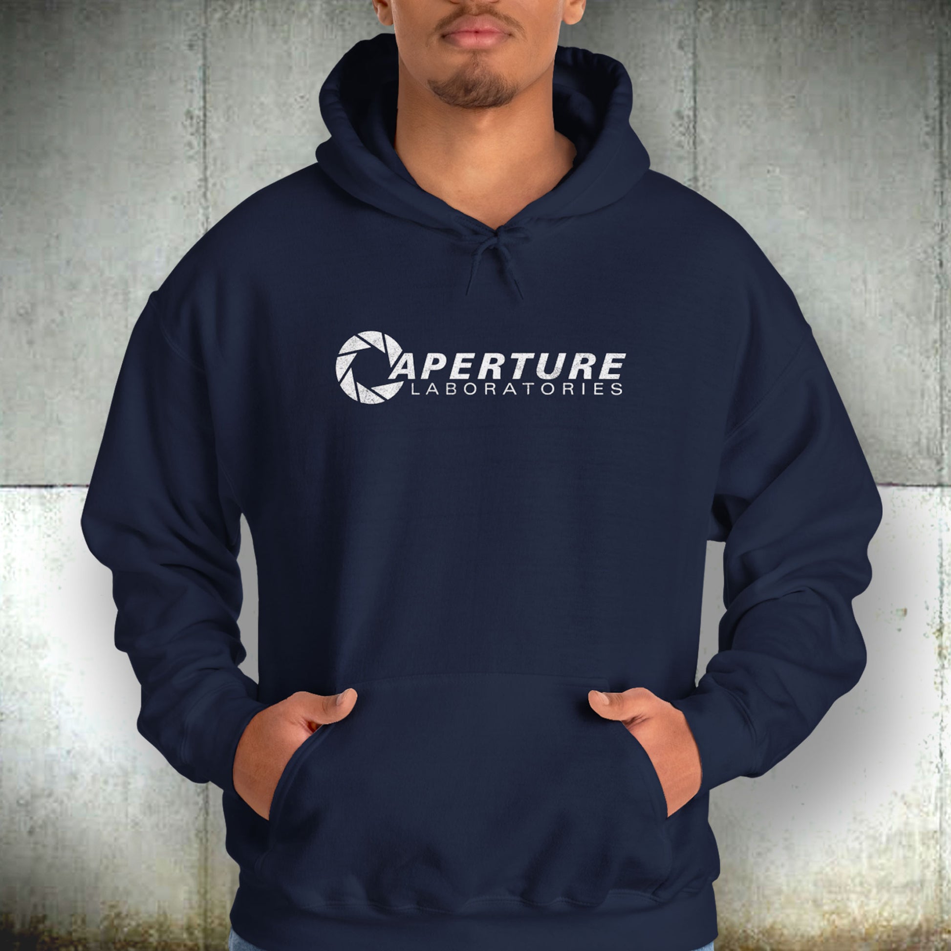 Male model wearing a navy blue colored Unisex Hoodie Heavy Blend Hooded Sweatshirt featuring the Aperture Laboratories logo from the video game Portal and Portal 2 in a vintage distressed style, sold by ScriptedBrand.