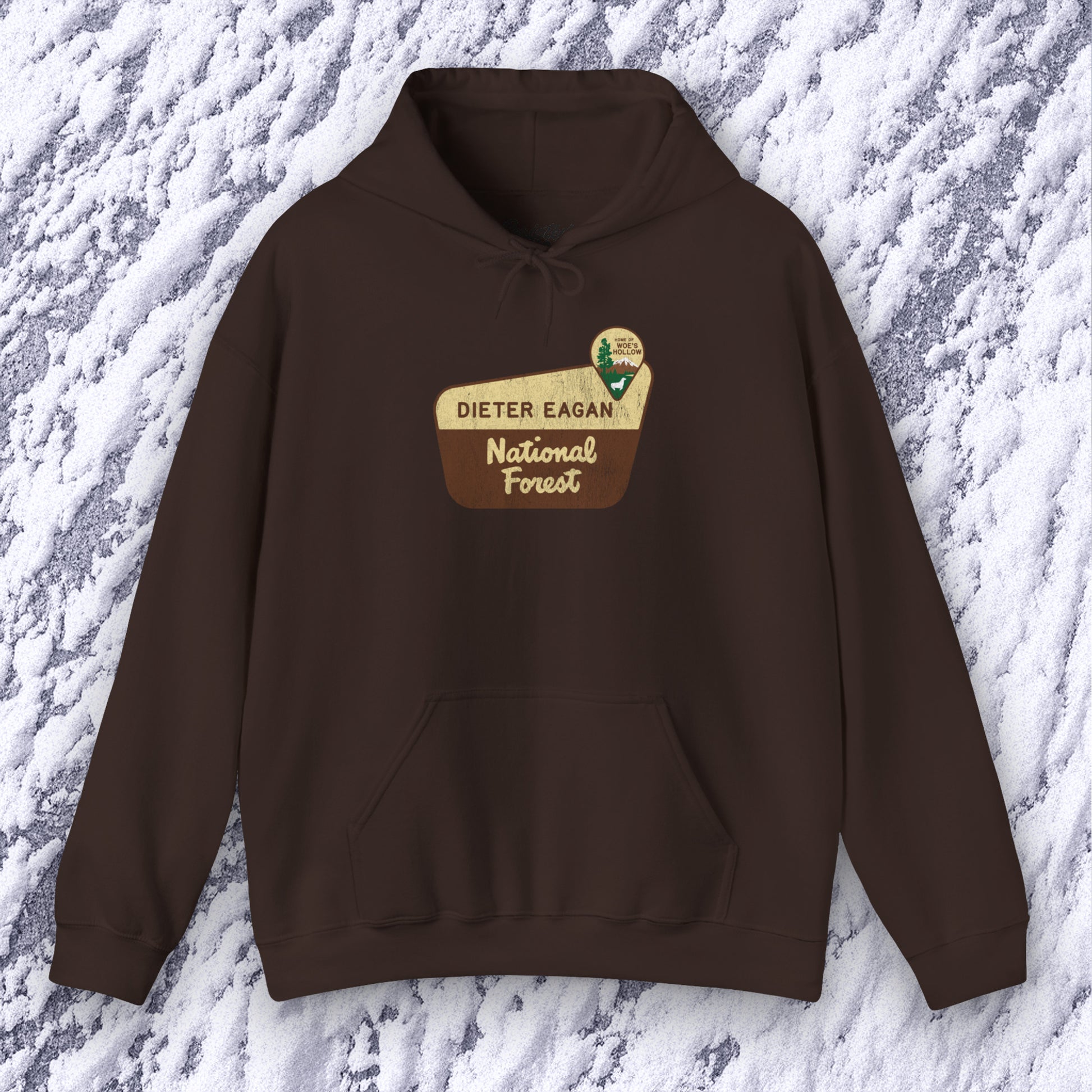 Mockup of a dark chocolate colored Soft Unisex Hoodie Heavy Blend Hooded Sweatshirt featuring the logo graphic of the Dieter Eagan National Forest inspired by the TV show Severance in a vintage distressed ink-stamped worn-in style.