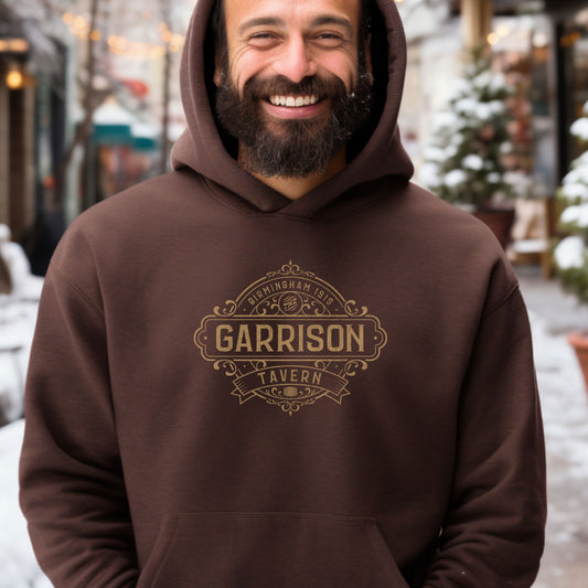 Male model wearing a dark chocolate Soft Unisex Hoodie Heavy Blend Hooded Sweatshirt featuring the Garrison Tavern Bar Logo Graphic inspired by the TV show and movie Peaky Blinders in a vintage distressed style.