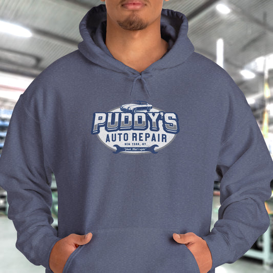 Male model wearing a heather navy blue soft Unisex Hoodie Heavy Blend Hooded Sweatshirt featuring a Puddy's Auto Repair graphic designed by ScriptedBrand inspired by the TV show Seinfeld in a vintage distressed style.