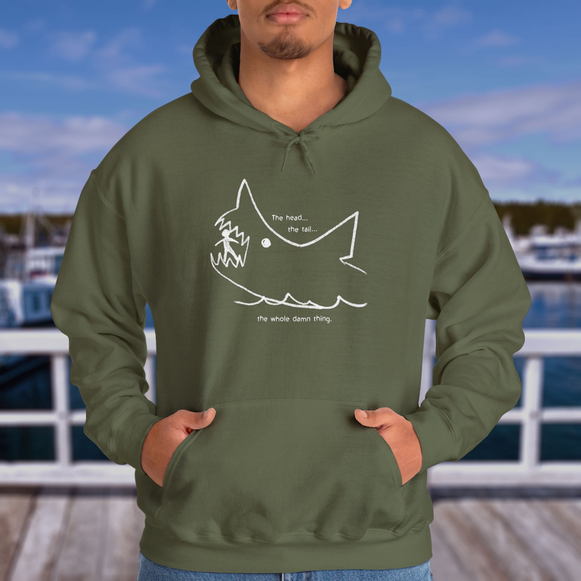 Male model wearing a Military Green colored Soft Unisex Hoodie Heavy Blend Hooded Sweatshirt with the chalkboard drawing of a shark eating a person, drawn by Quint in the movie Jaws.