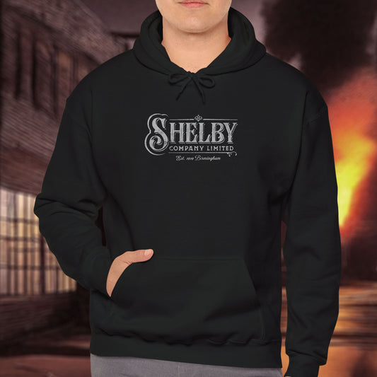 Male model wearing a black colored Soft Unisex Hoodie Heavy Blend Hooded Sweatshirt featuring the fictional logo Shelby Company Limited from the TV series Peaky Blinders in a vintage distressed style.