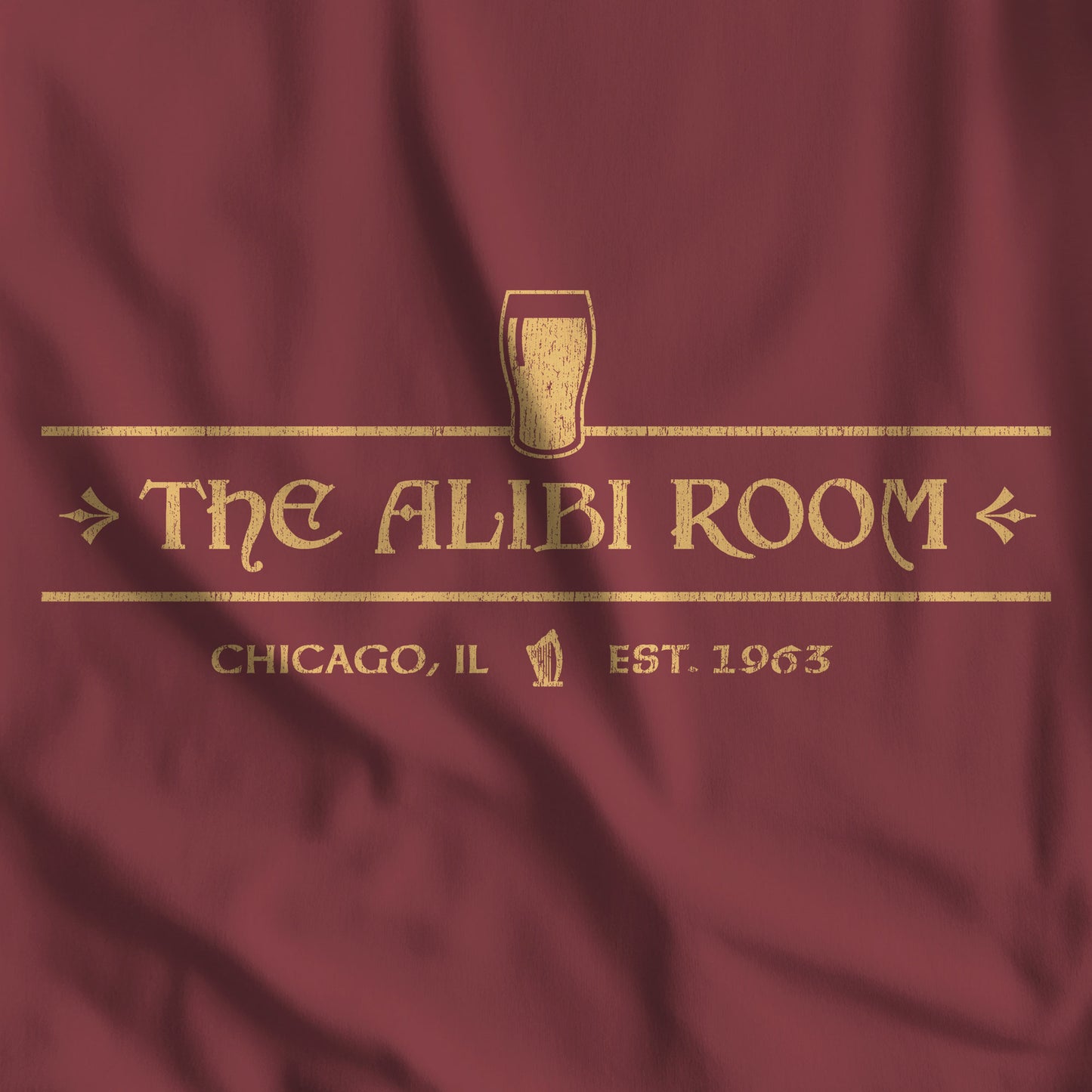 Closeup of maroon t-shirt featuring gold The Alibi Room logo graphic inspired by the TV show Shameless in a vintage distressed style.