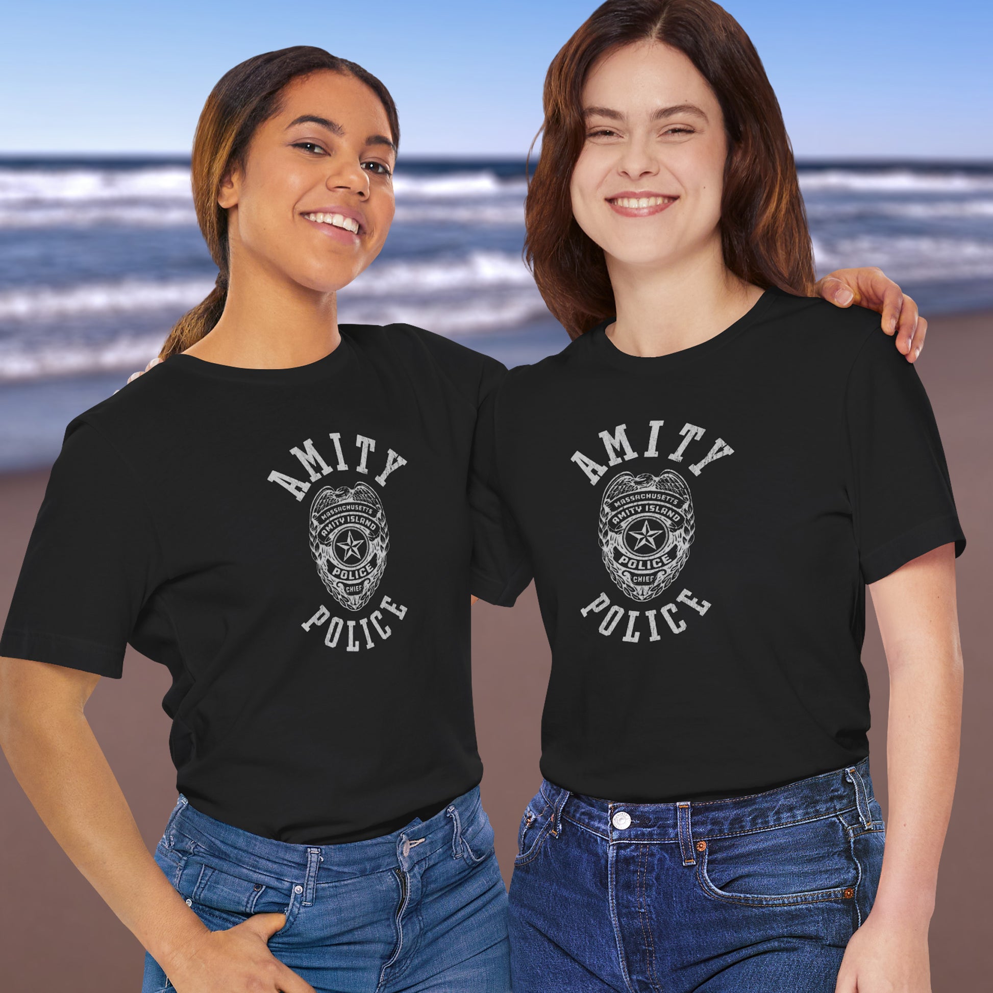 2 female models wearing black colored Soft unisex Bella+Canvas 3001 short-sleeve t-shirts featuring an Amity Island Police logo graphic, designed by ScriptedBrand, and  inspired by the movie Jaws in a vintage distressed style.