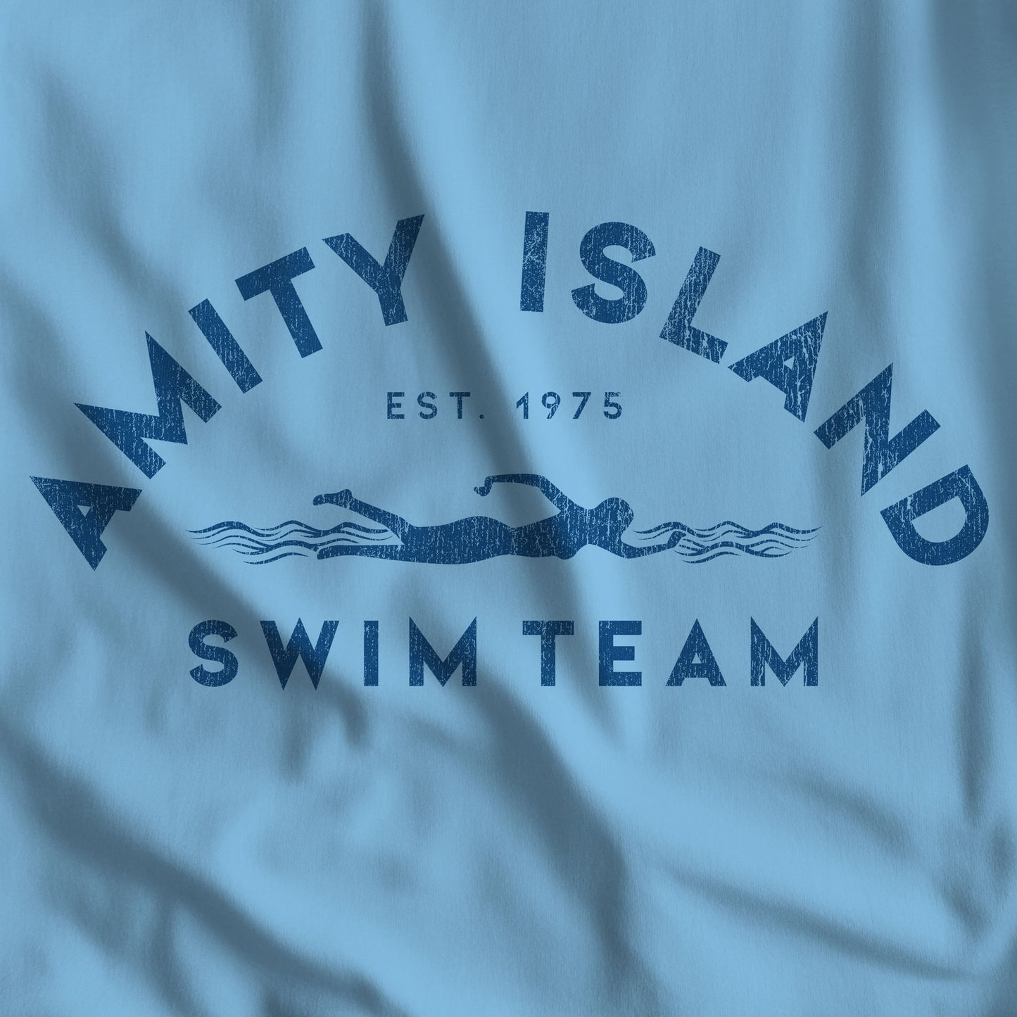 Closeup of ocean blue t-shirt featuring an Amity Island Swim Team logo graphic inspired by the movie Jaws in a vintage distressed style.