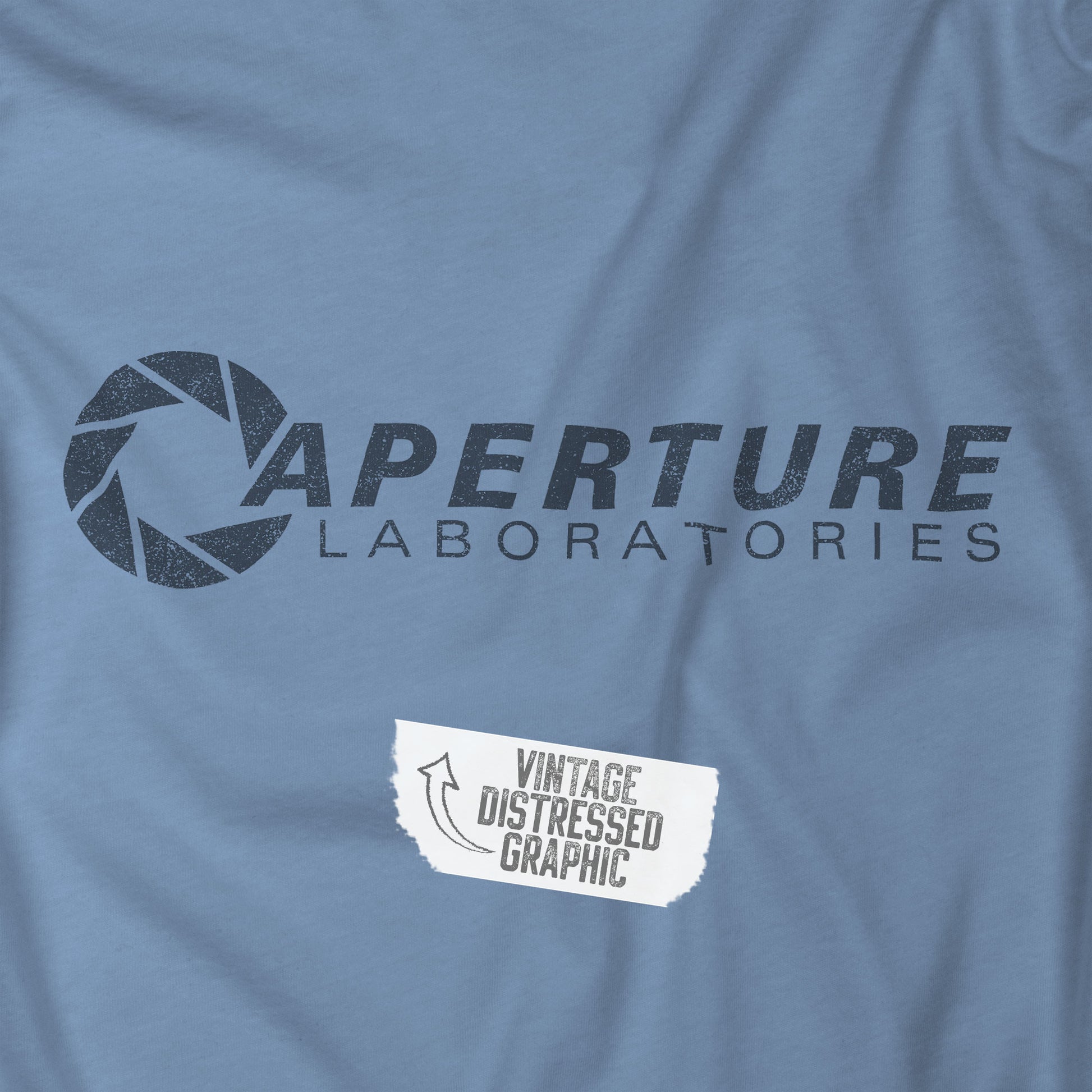Closeup view of a steel blue colored soft Bella+Canvas t-shirt with the Aperture Laboratories logo from the video game Portal and Portal 2 in a vintage ink-stamped distressed style. 
