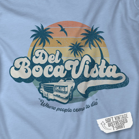Closeup of a baby blue Soft Bella+Canvas 3001 short-sleeve t-shirt featuring a Del Boca Vista logo graphic (uniquely designed by ScriptedBrand), including the phrase Where People Come To Die, inspired by the TV show Seinfeld, in a vintage distressed style.