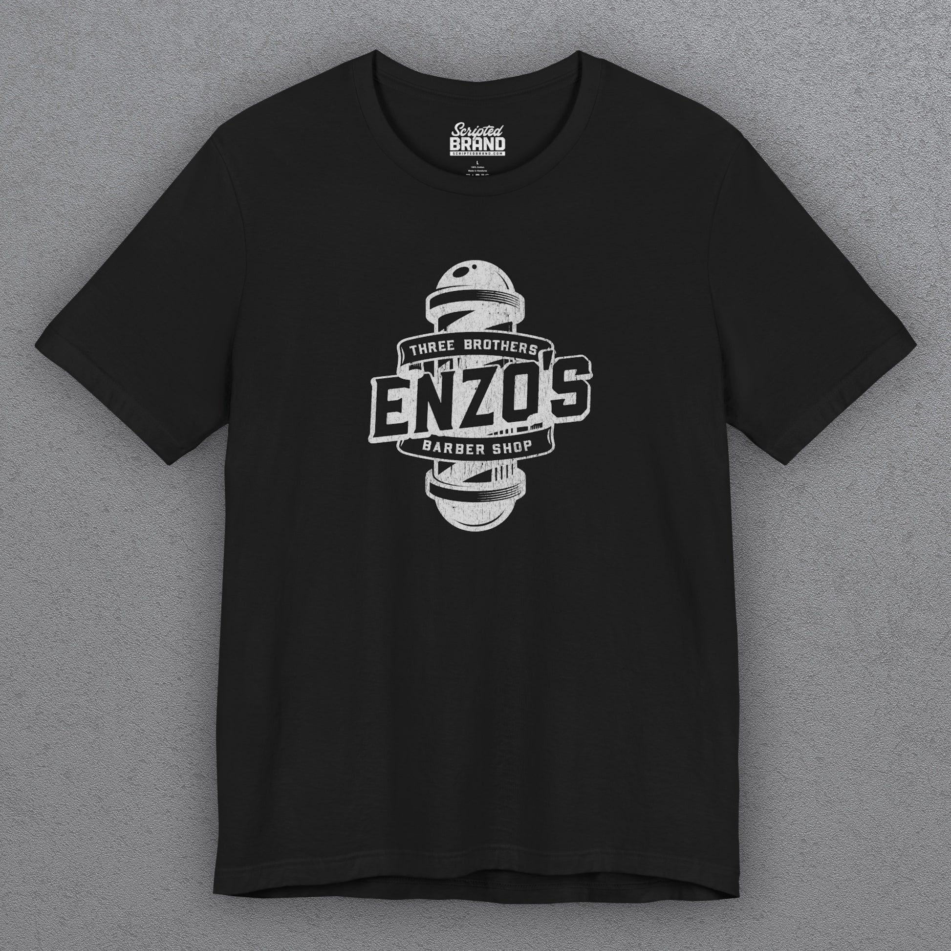 Front view of a black t-shirt with the Enzo's Barber Shop logo graphic inspired by the TV show Seinfeld in a vintage distressed style.