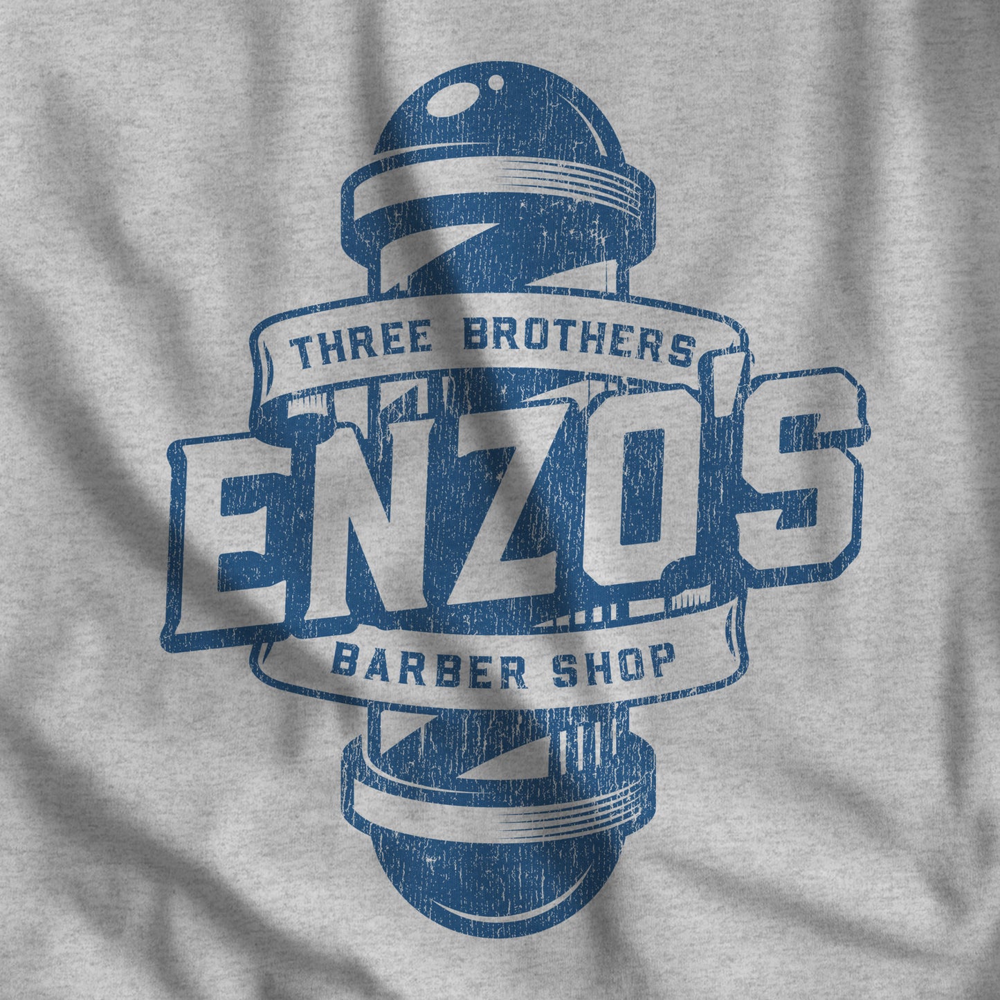 Closeup of athletic heather gray t-shirt with the Enzo's Barber Shop logo graphic inspired by the TV show Seinfeld in a vintage distressed style.