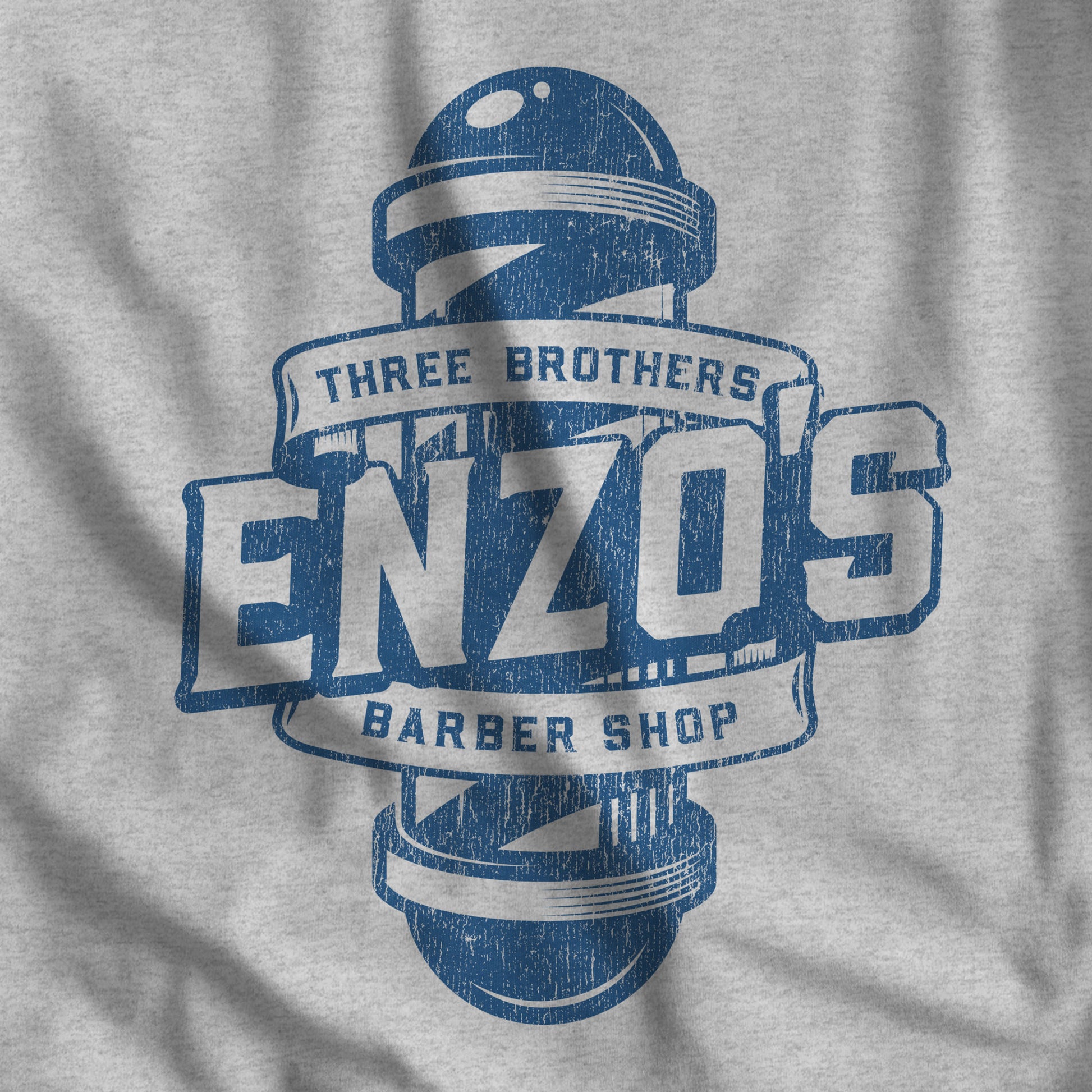 Closeup of athletic heather gray t-shirt with the Enzo's Barber Shop logo graphic inspired by the TV show Seinfeld in a vintage distressed style.