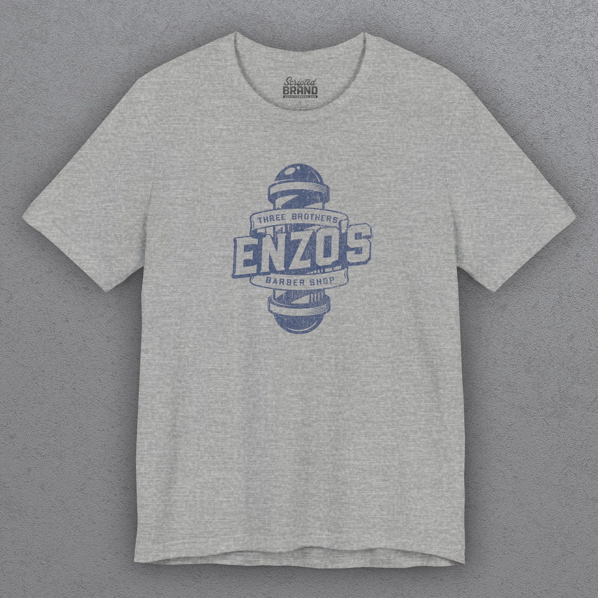 Front view of an athletic heather gray t-shirt with the Enzo's Barber Shop logo graphic inspired by the TV show Seinfeld in a vintage distressed style.