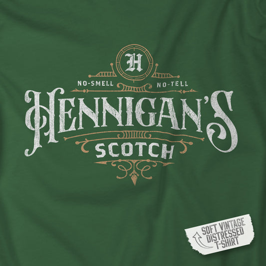 Closeup view of an Evergreen colored soft short-sleeve t-shirt featuring a Hennigans Scotch Whisky logo graphic inspired by the TV show Seinfeld in a vintage distressed ink-stamped worn-in style.
