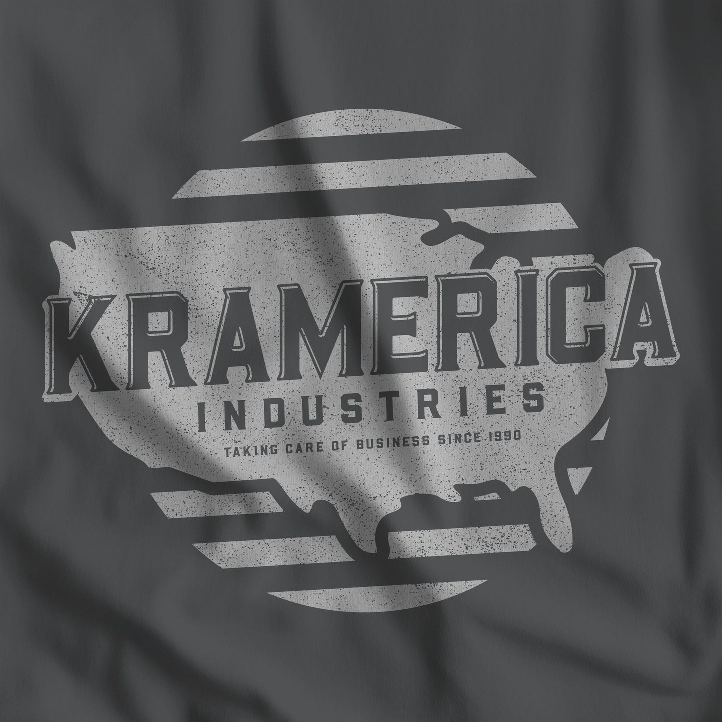 Closeup of Asphalt dark gray t-shirt featuring a Kramerica logo graphic inspired by the TV show Seinfeld in a vintage distressed style.