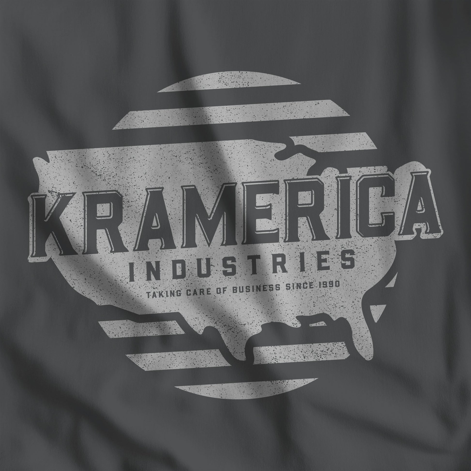 Closeup of Asphalt dark gray t-shirt featuring a Kramerica logo graphic inspired by the TV show Seinfeld in a vintage distressed style.