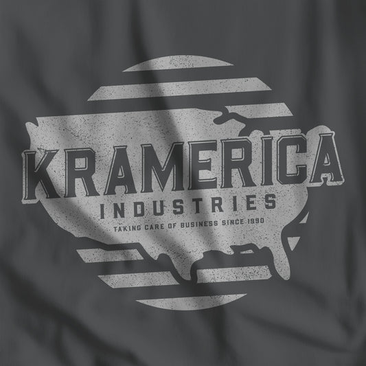 Closeup of Asphalt dark gray t-shirt featuring a Kramerica logo graphic inspired by the TV show Seinfeld in a vintage distressed style.