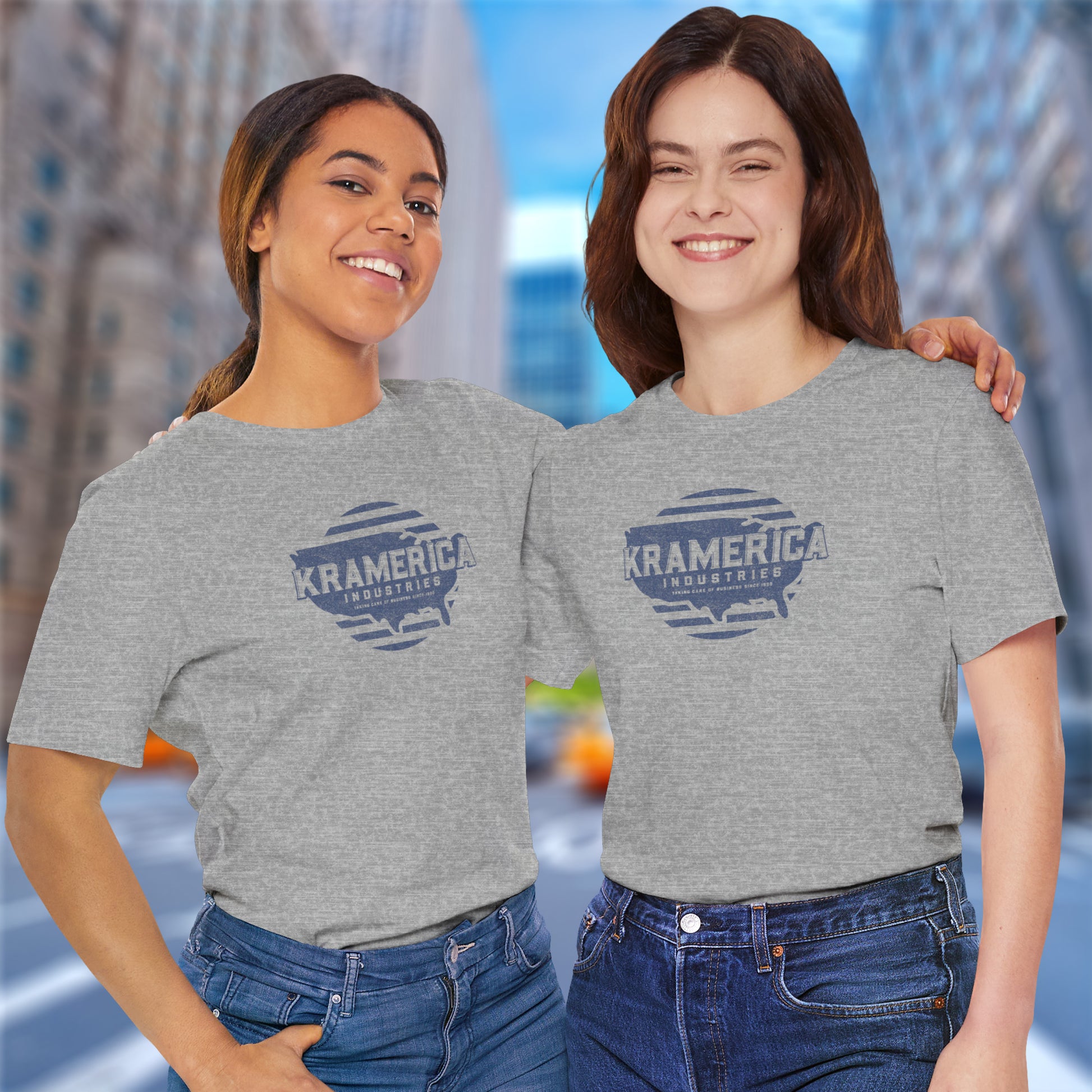 Two women wearing heather gray t-shirts featuring a Kramerica logo graphic inspired by the TV show Seinfeld in a vintage distressed style.